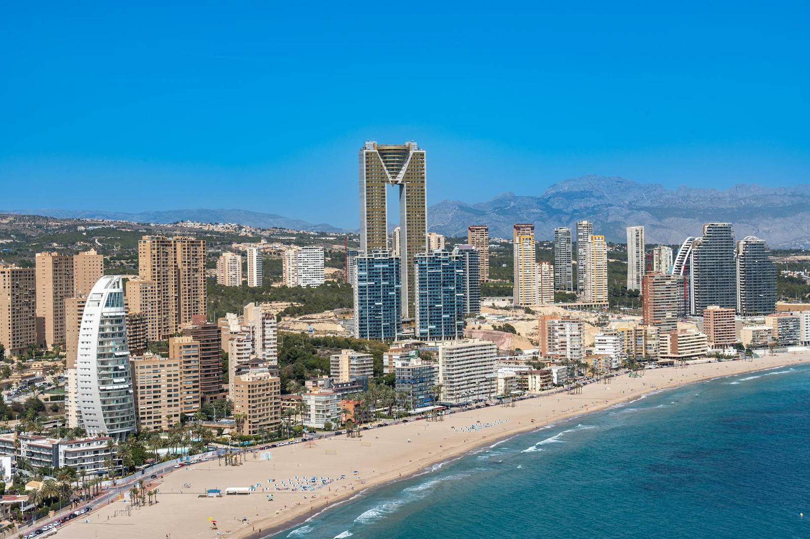 Aerial view of a beachfront skyline with a slender twisted skyscraper among the towers