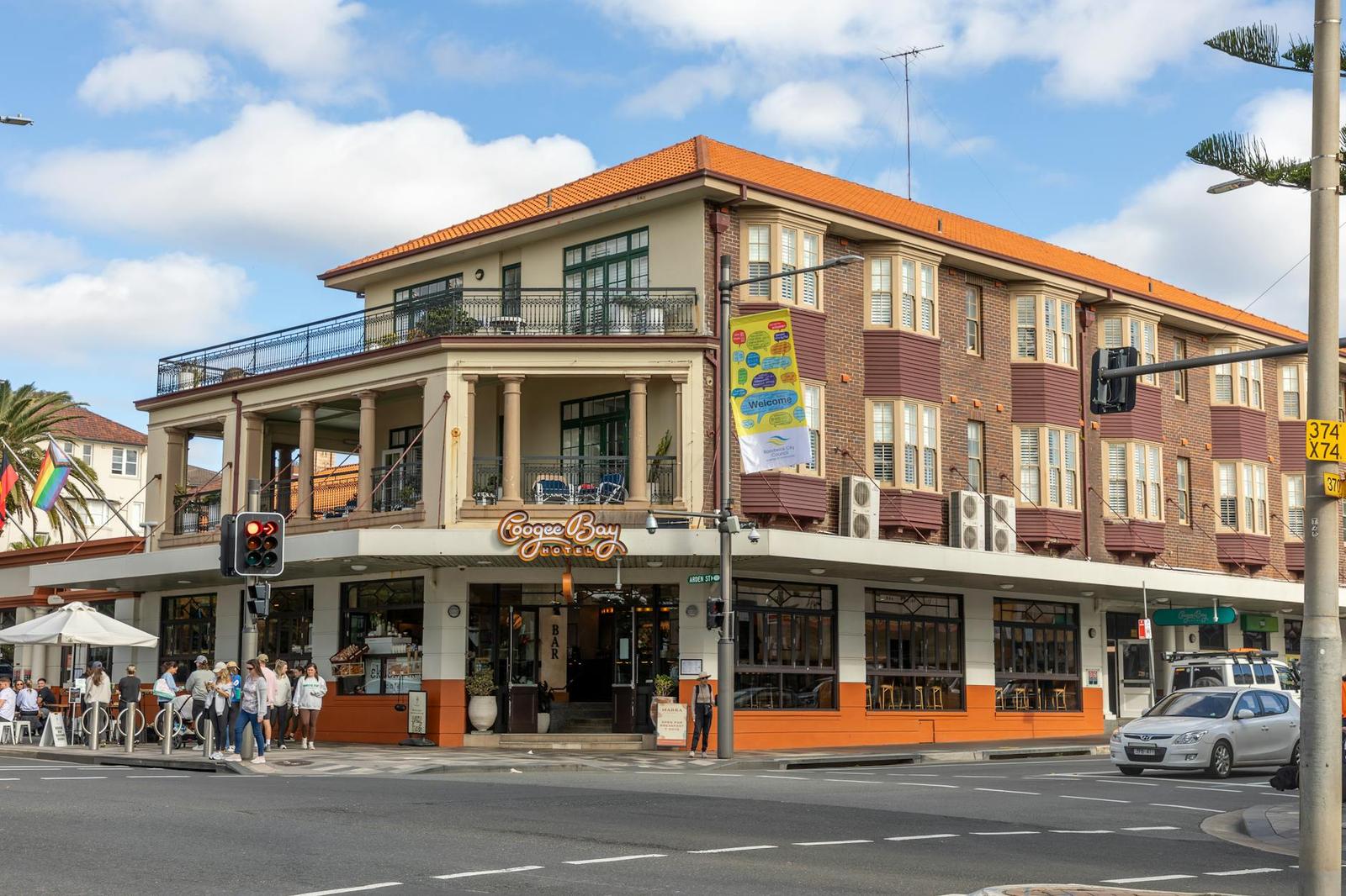 A three-storey corner hotel with balconies and a street-level cafe crowd