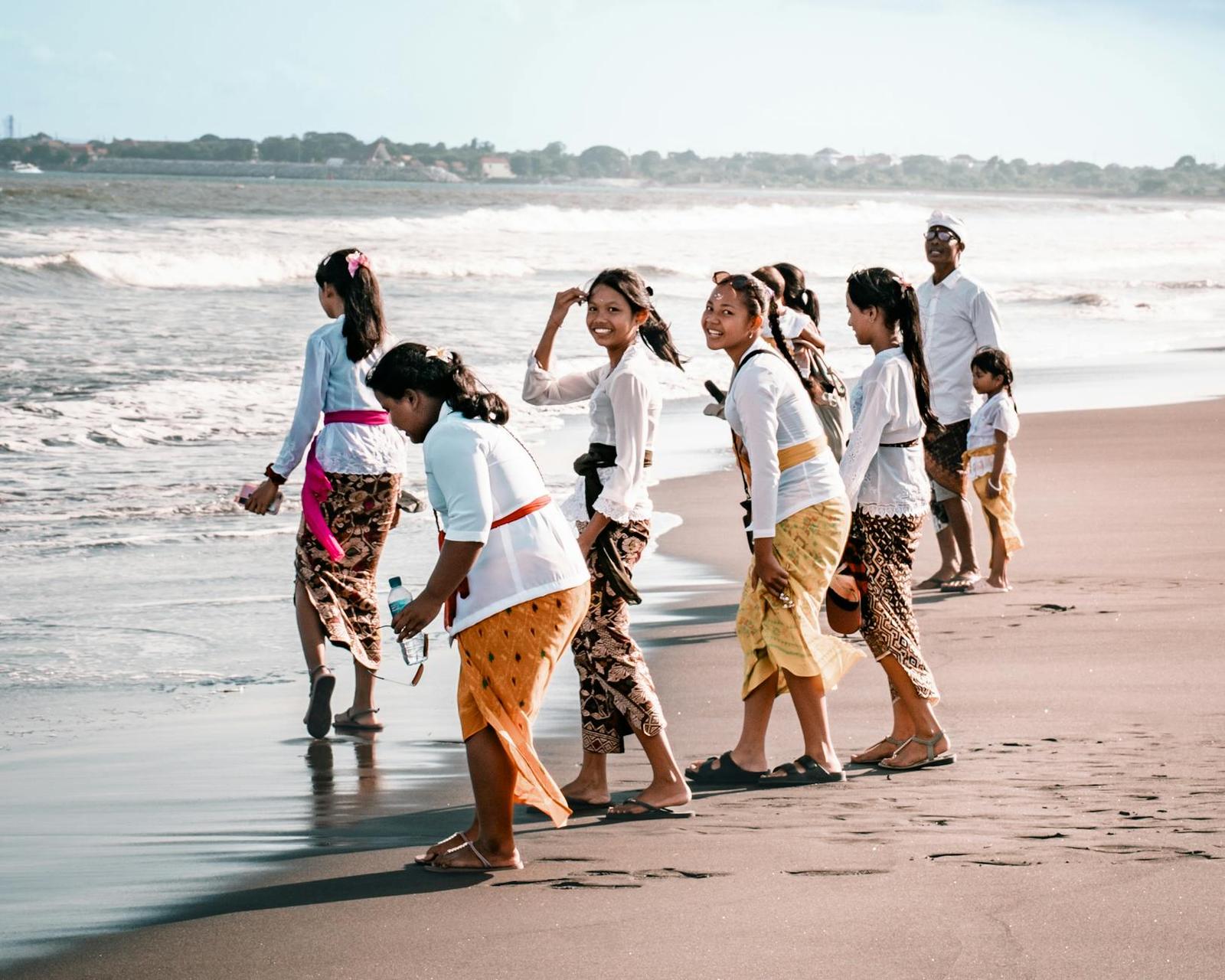 A group in traditional white and gold ceremonial dress walking along the shore