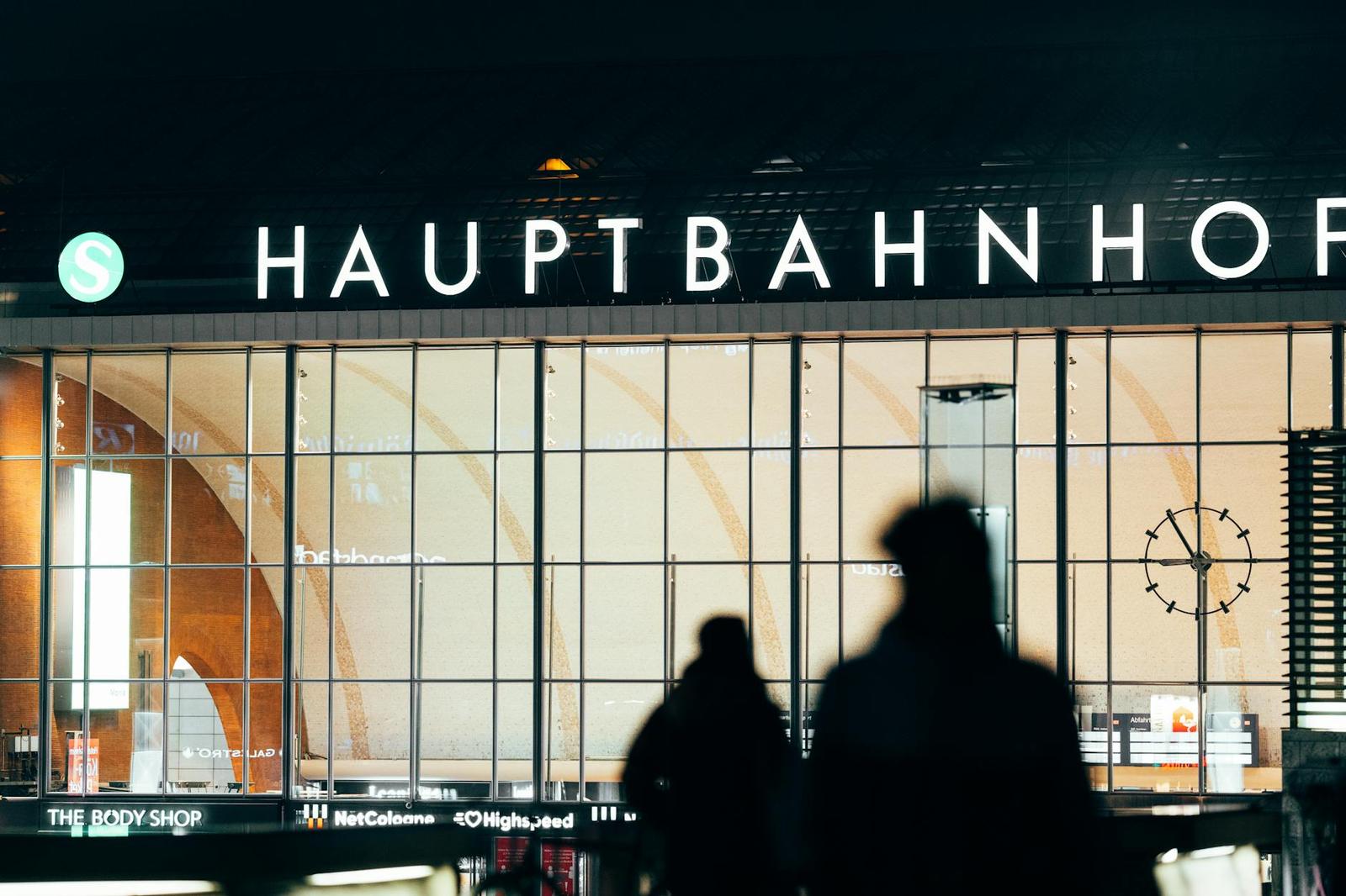 Silhouetted travellers passing an illuminated train station facade at night