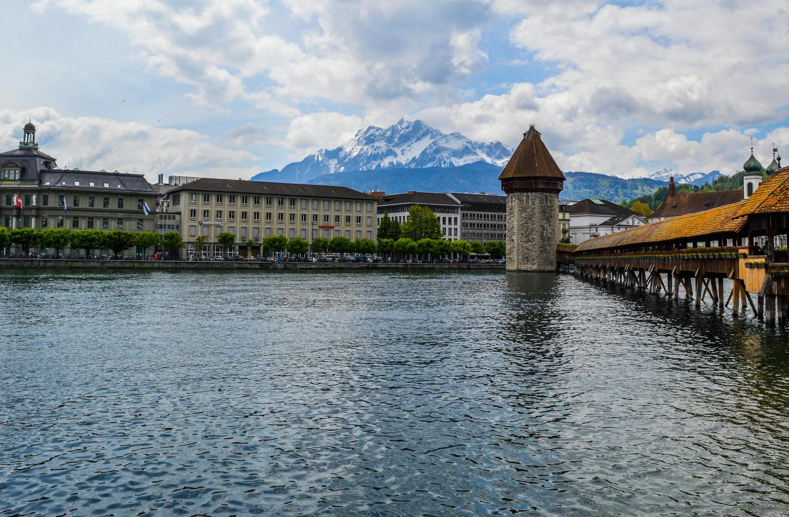 Riverside old town with a wooden covered bridge and a snow-capped peak beyond