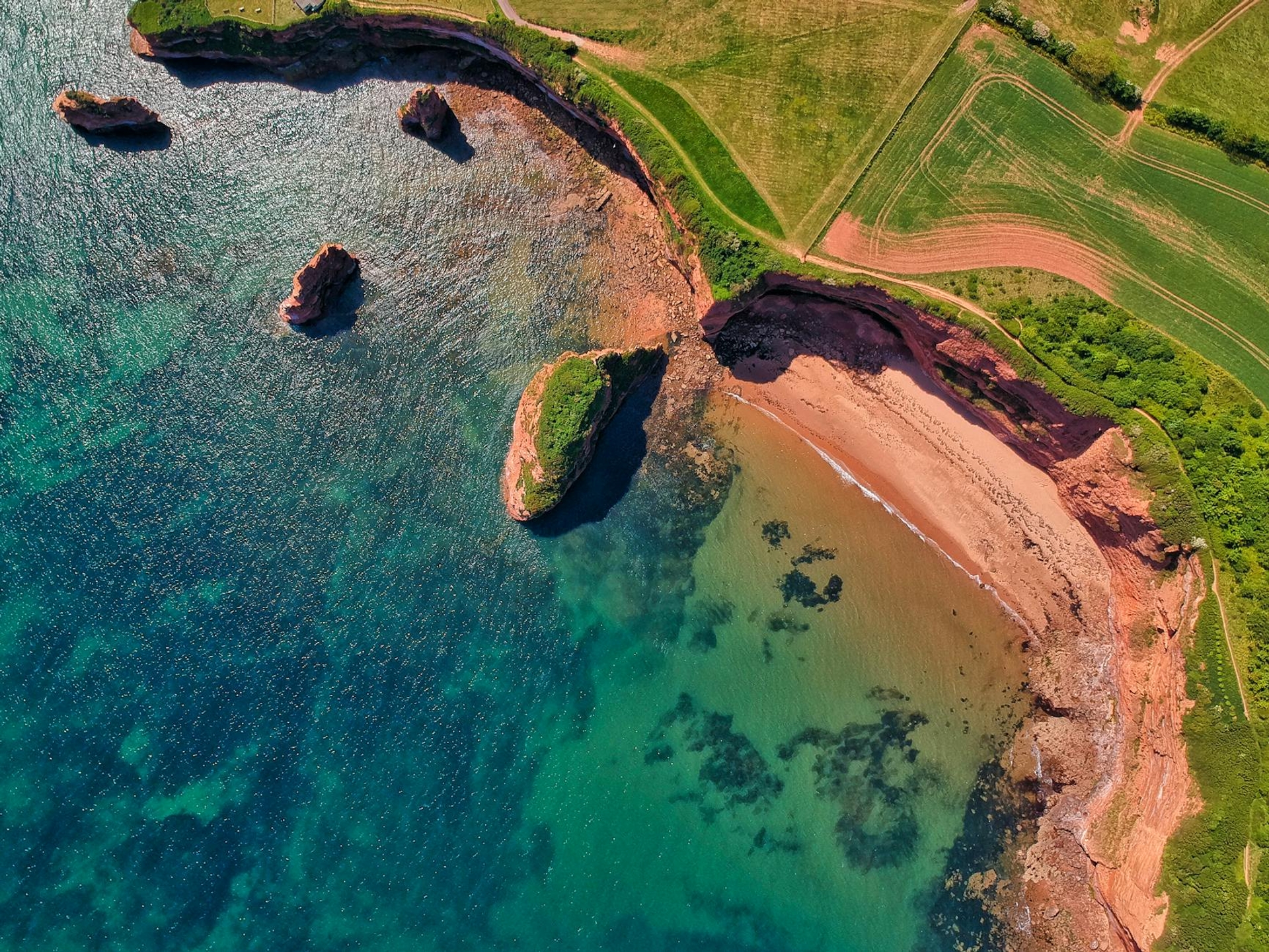 Aerial view of red sandstone cliffs meeting turquoise coastal water