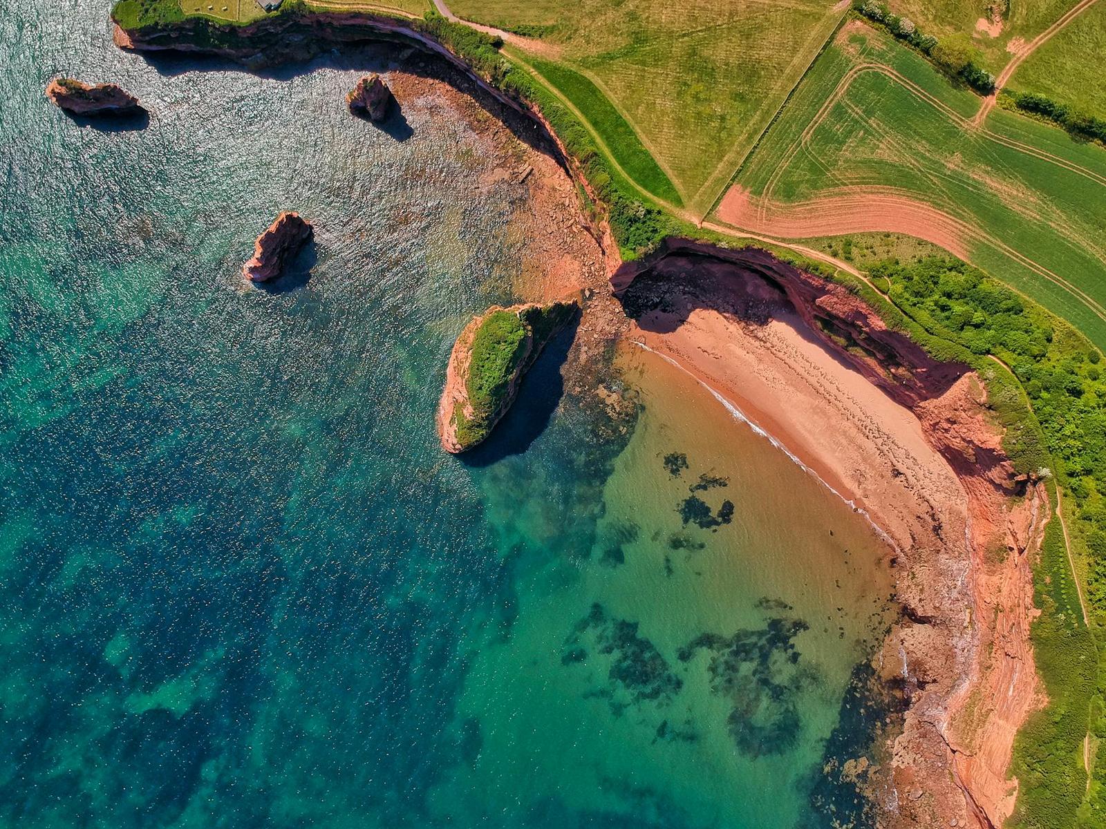 Aerial view of red sandstone cliffs meeting turquoise coastal water