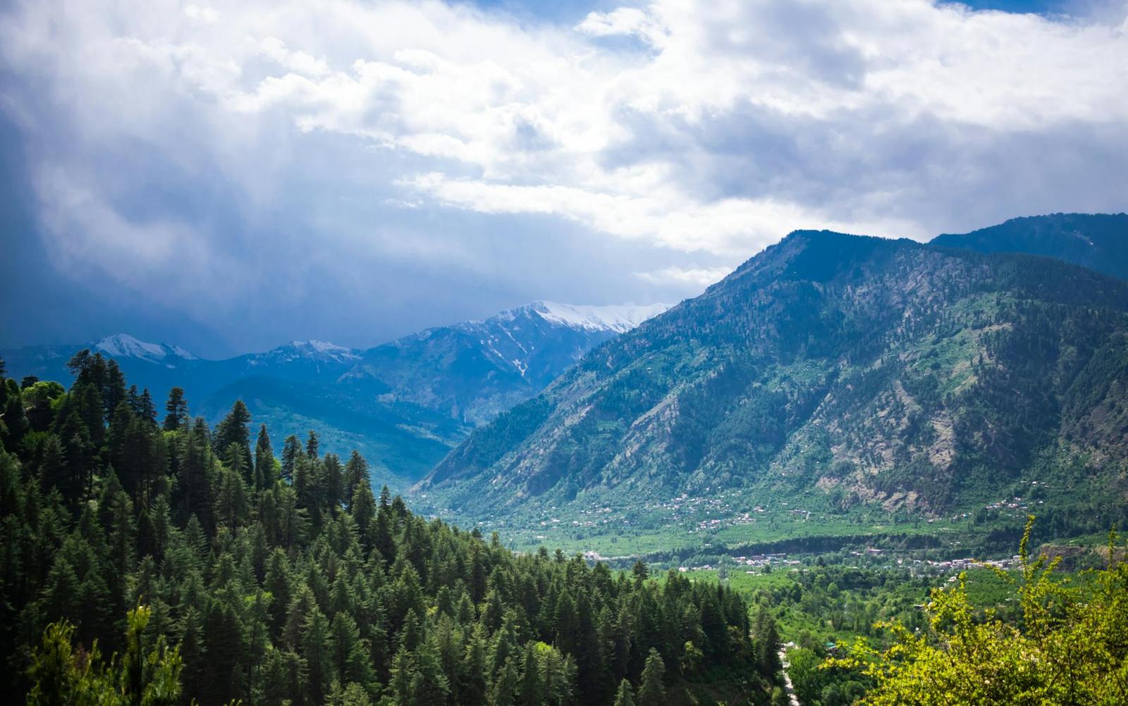 A forested river valley below cloud-wrapped mountains
