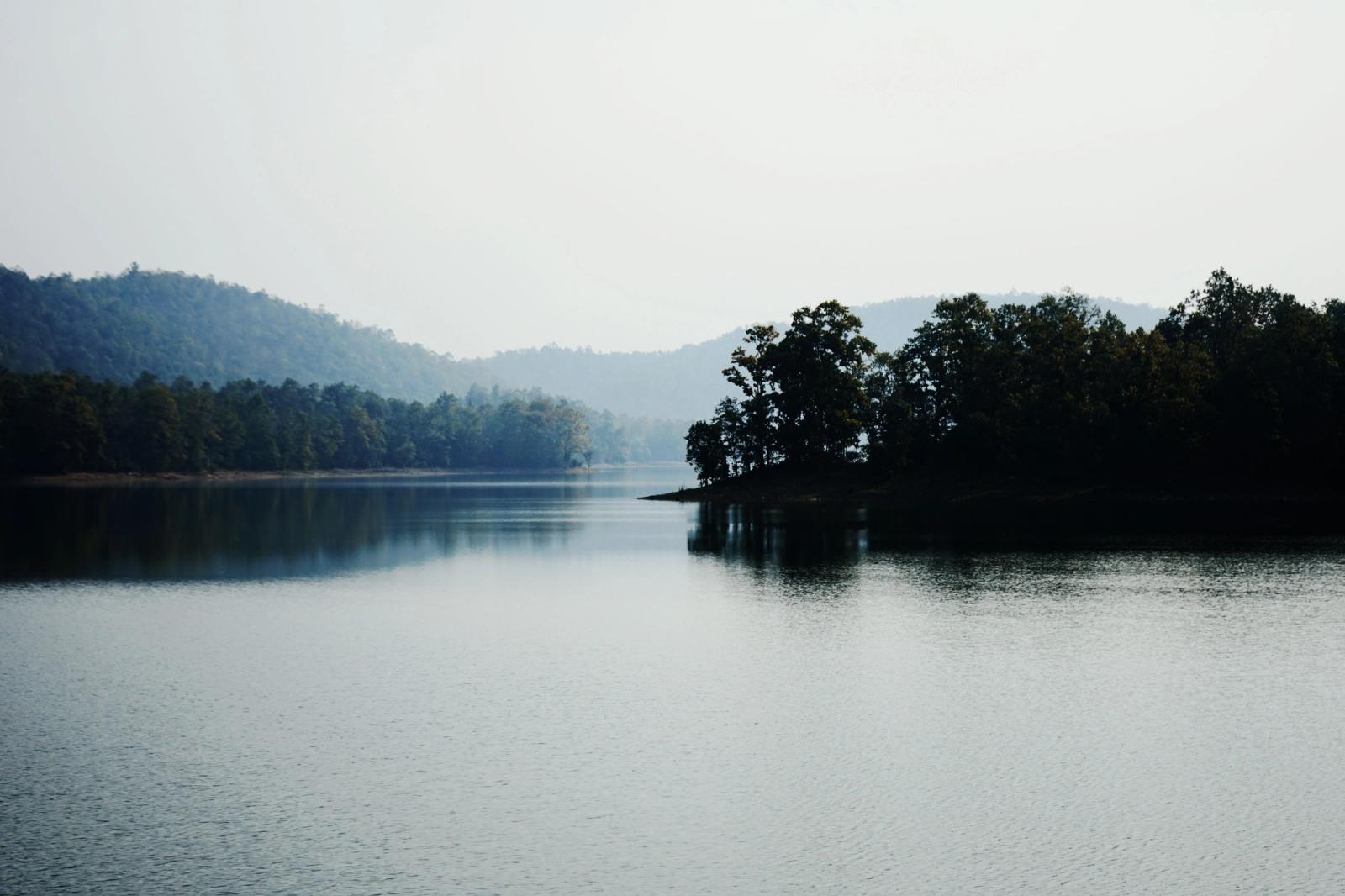 A calm lake bordered by forested hills fading into haze