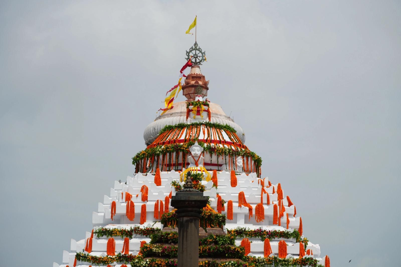 A beautifully decorated Indian temple dome with vibrant flowers and flags under a clear sky