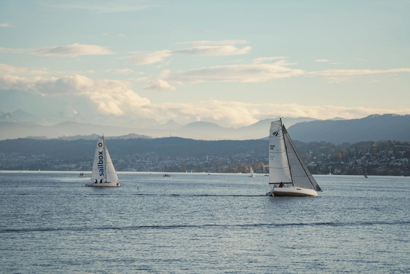 Sailboats gliding on a serene lake with picturesque mountain background under a gentle sky