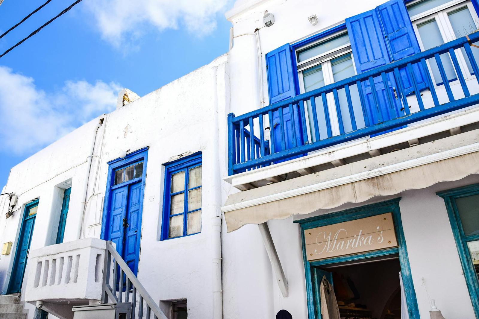 A whitewashed house with blue shutters and balcony above a shopfront
