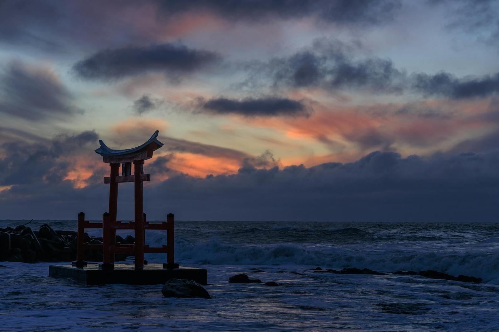 A wooden torii gate silhouetted against a fiery sunset over the sea