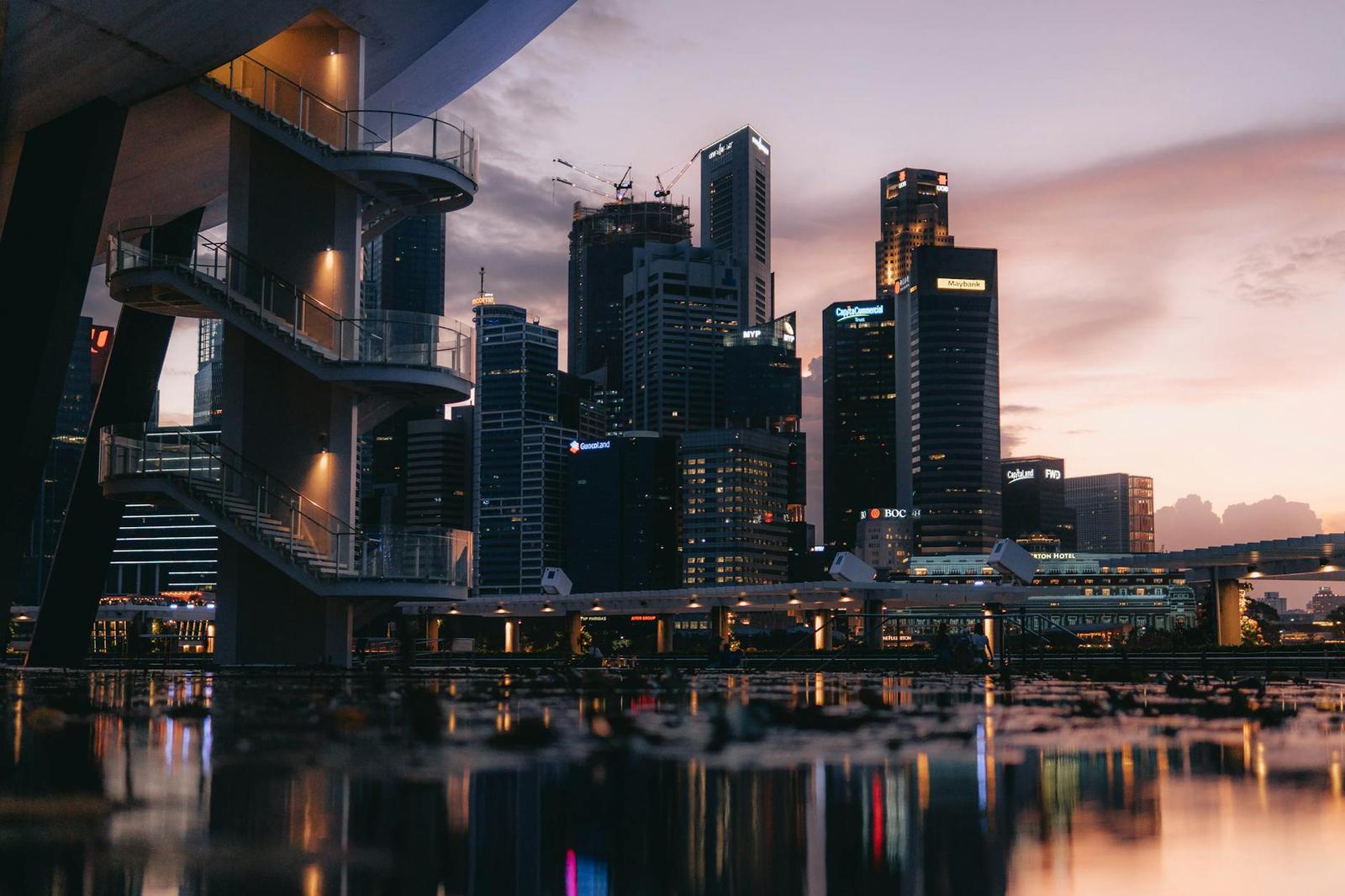 A city skyline reflected in still water beside a spiral staircase at twilight