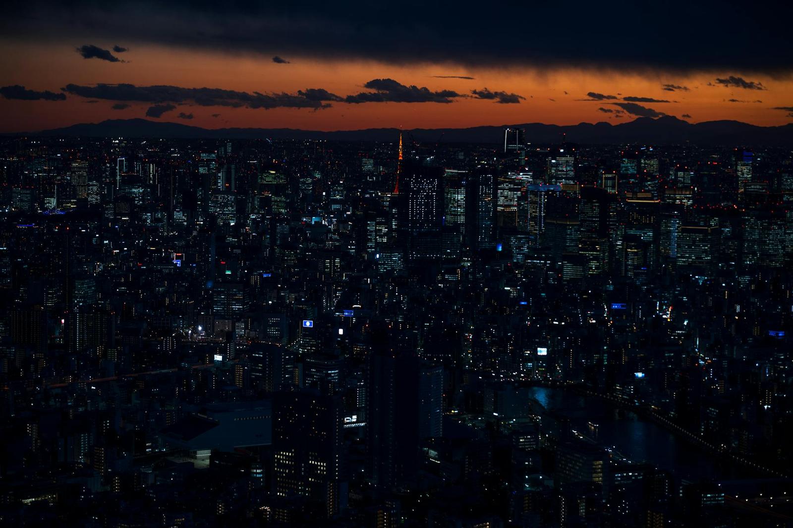 A vast city skyline at dusk with a single lit tower standing out