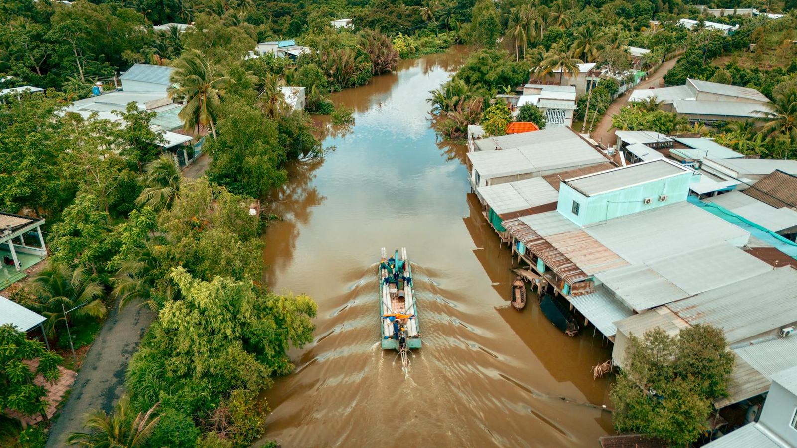 Aerial view of a tour boat cruising a muddy river past a village