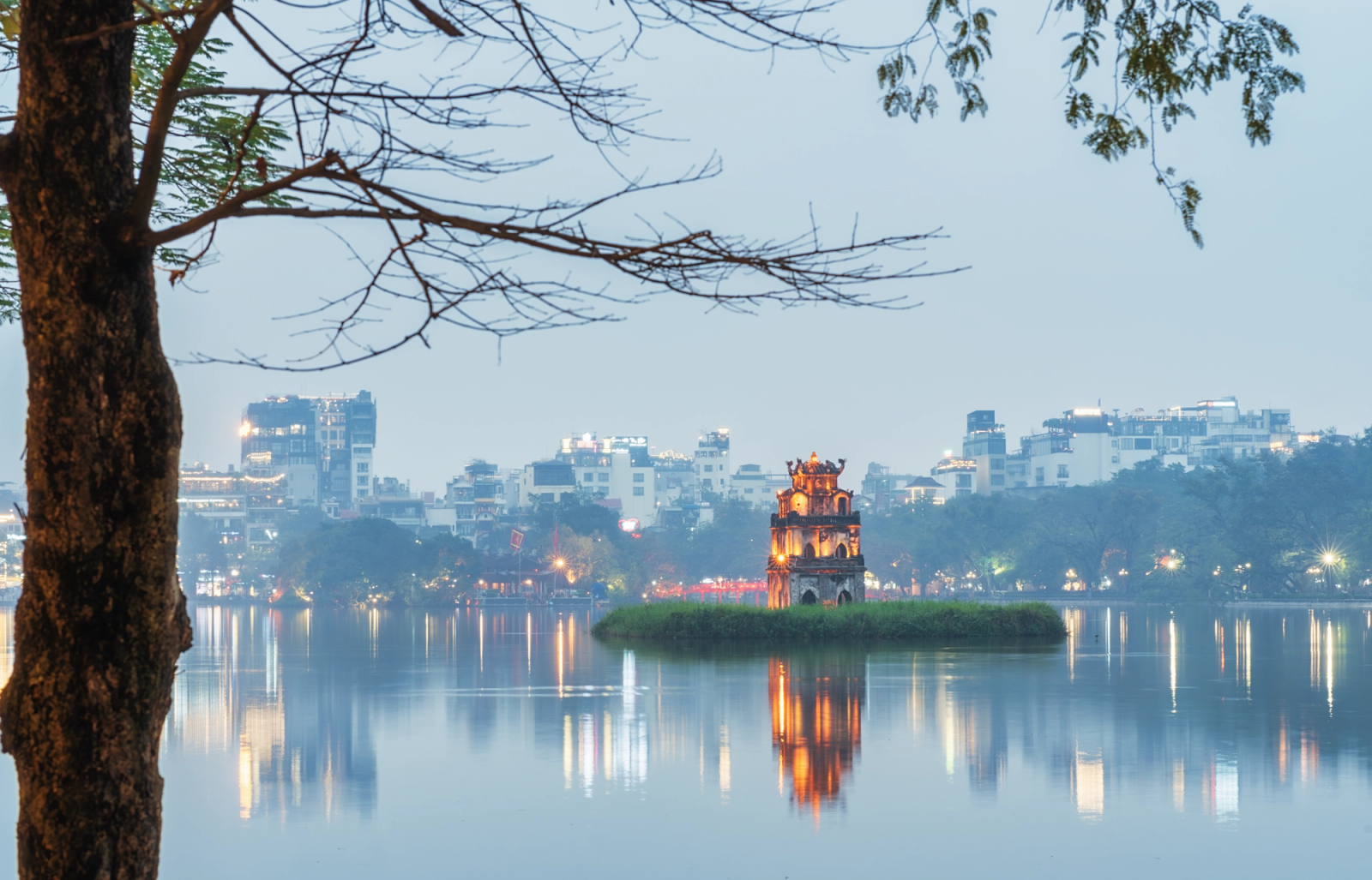 Serene view of the illuminated Turtle Tower on Hoan Kiem Lake in Hanoi during the evening, surrounded by city lights
