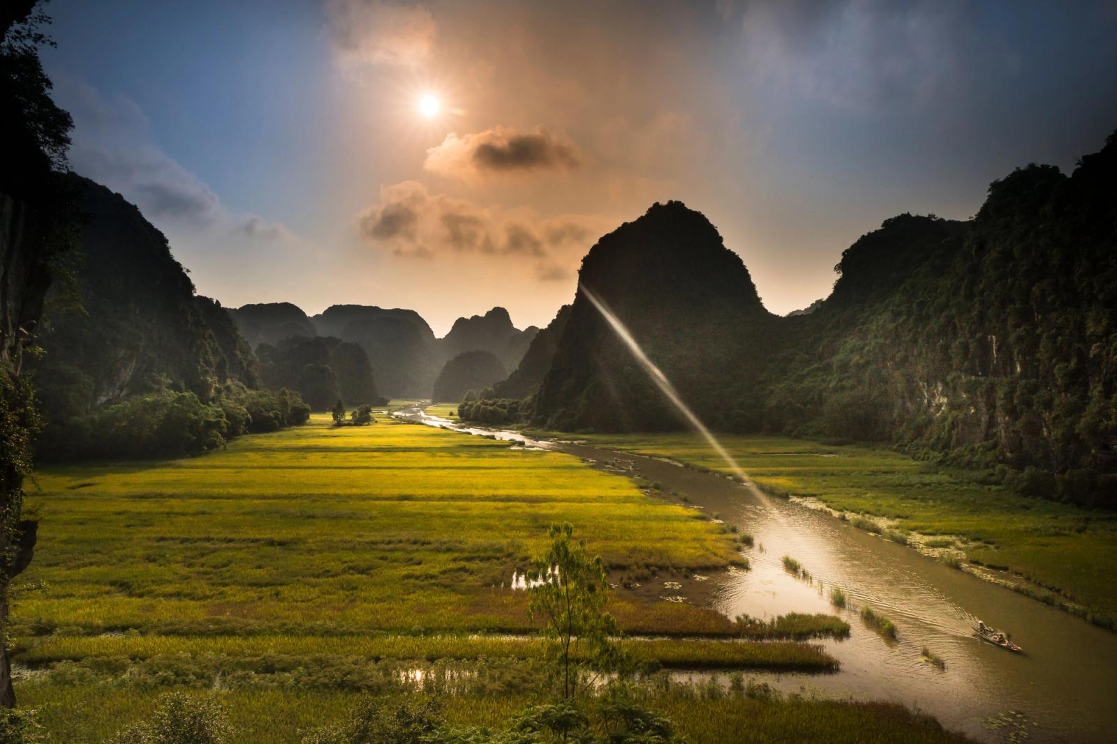 Stunning sunset view over rice fields and river in Ninh Binh, Vietnam, with dramatic sunrays and karst formations