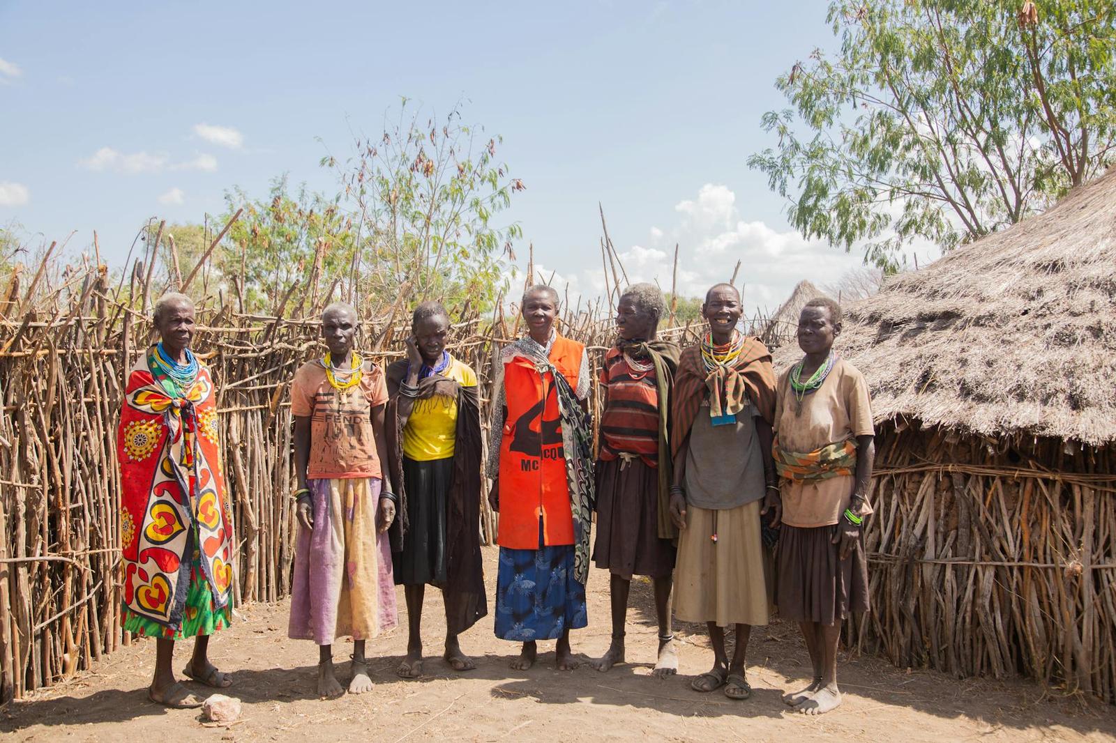 A group of women in colorful wraps standing outside thatched huts