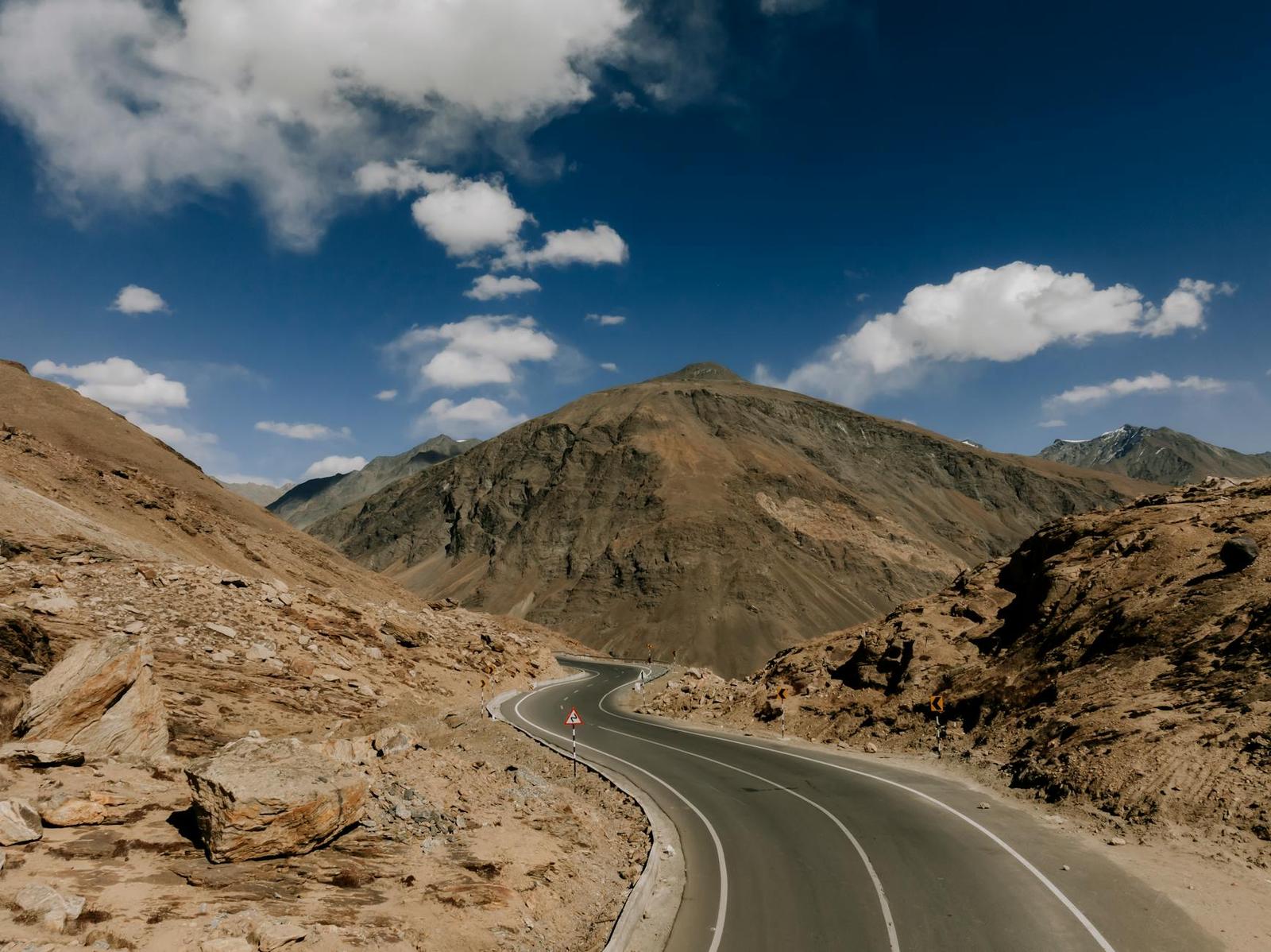Paved mountain road curving through arid rocky peaks under a blue sky