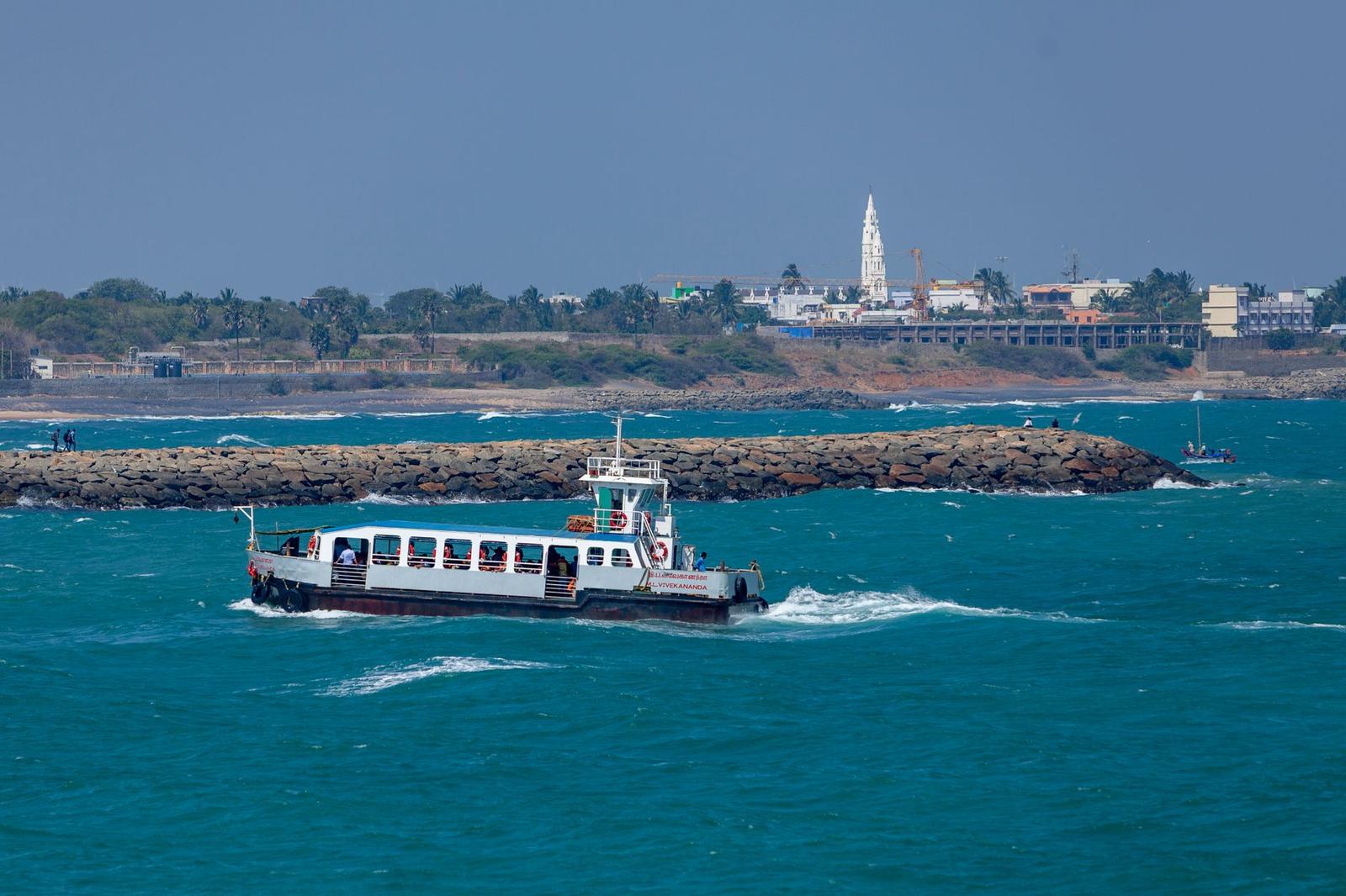 Passenger boat sailing near Kanyakumari coast with view of distant city and waves