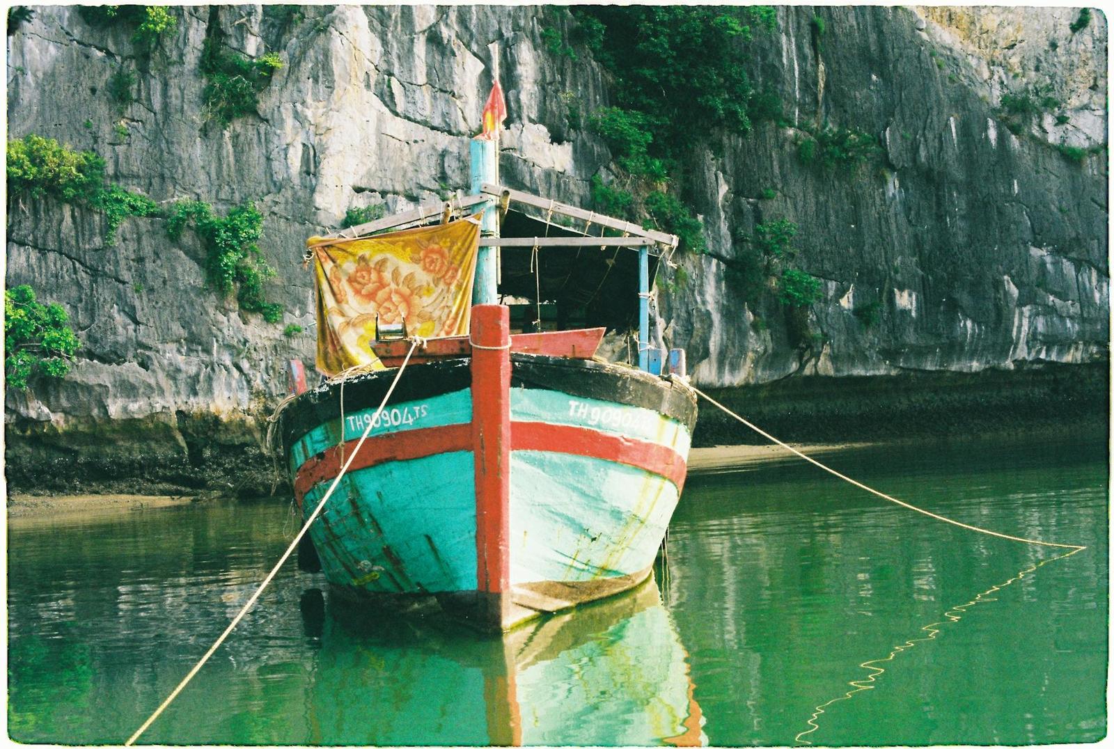 A colorful wooden boat moored by a limestone cliff in a bay in Vietnam