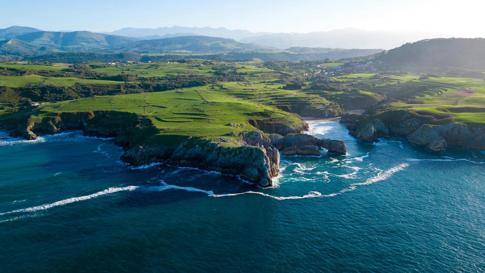 Aerial view of green farmland meeting rugged cliffs along a coastline