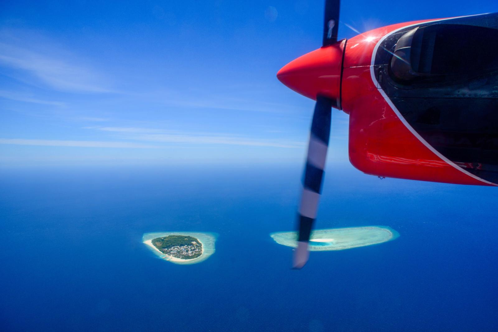 Seaplane flying over tropical islands in Maldives, showcasing clear blue ocean and sky