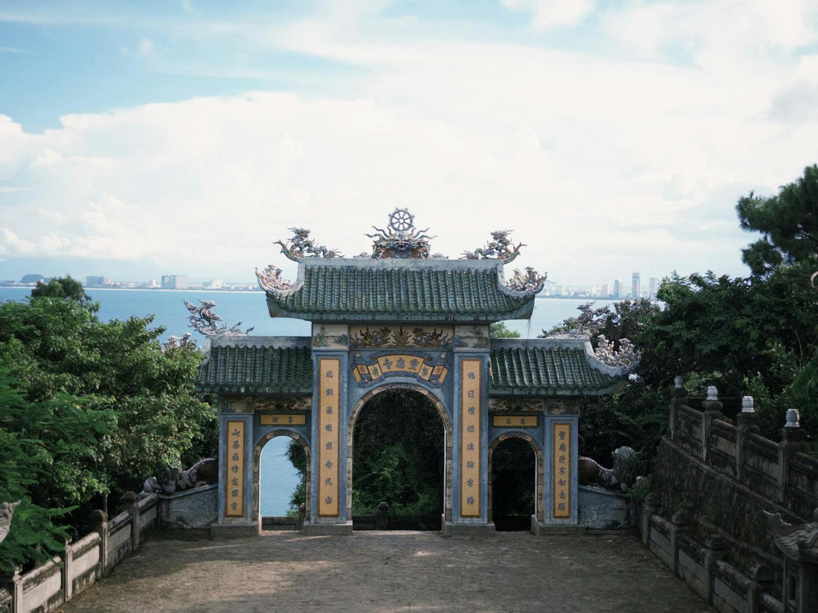 An ornate stone temple gateway overlooking the sea from a hillside