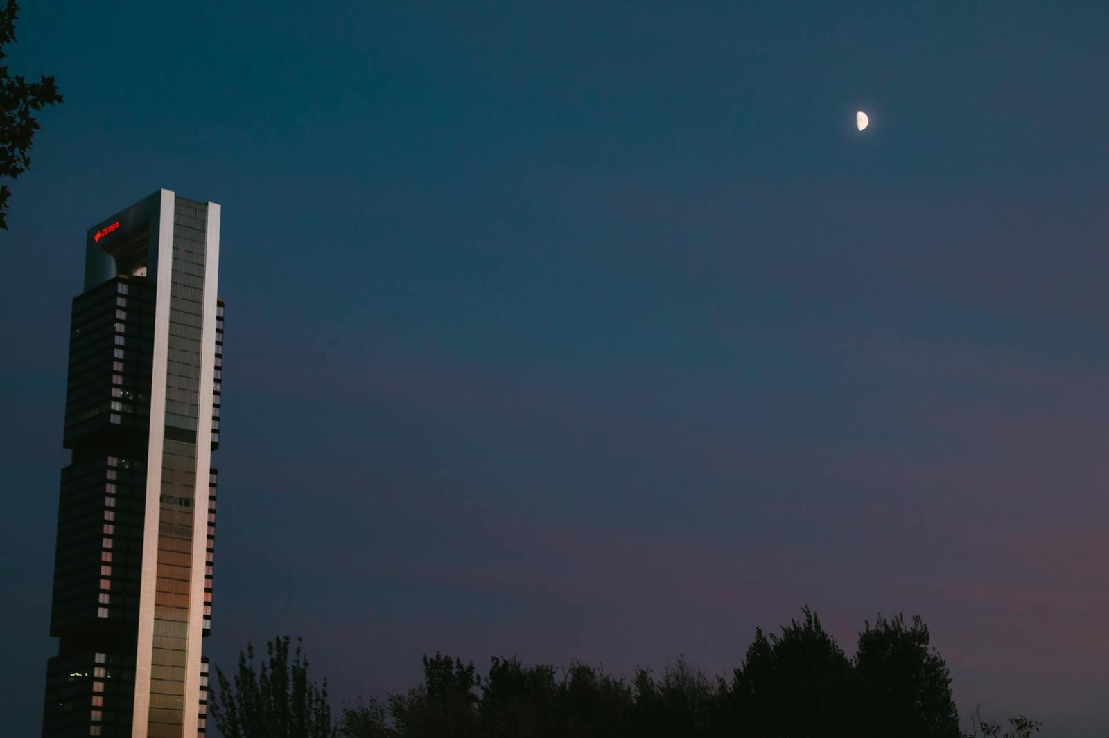 Illuminated tower block standing against a dusk sky with a rising moon
