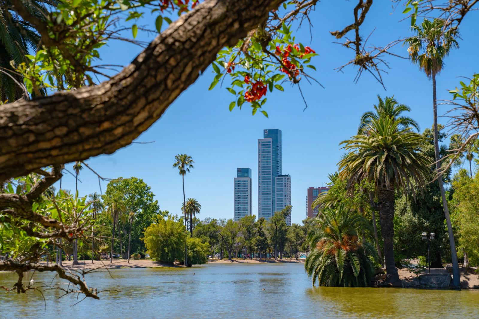 A tranquil park scene in Buenos Aires, featuring a lake, trees, and the city skyline