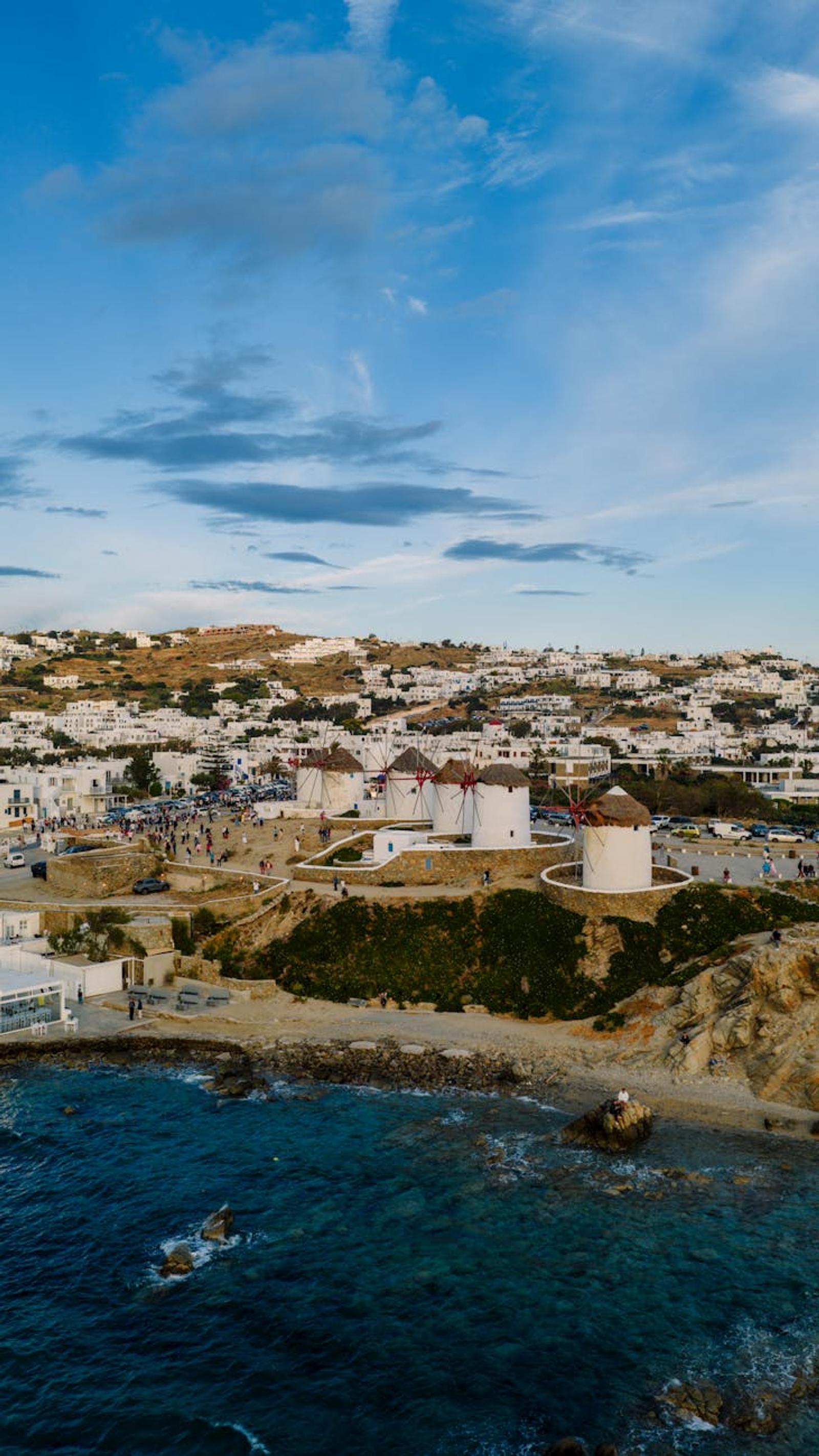 Aerial view of round white windmills above a rocky coastal town
