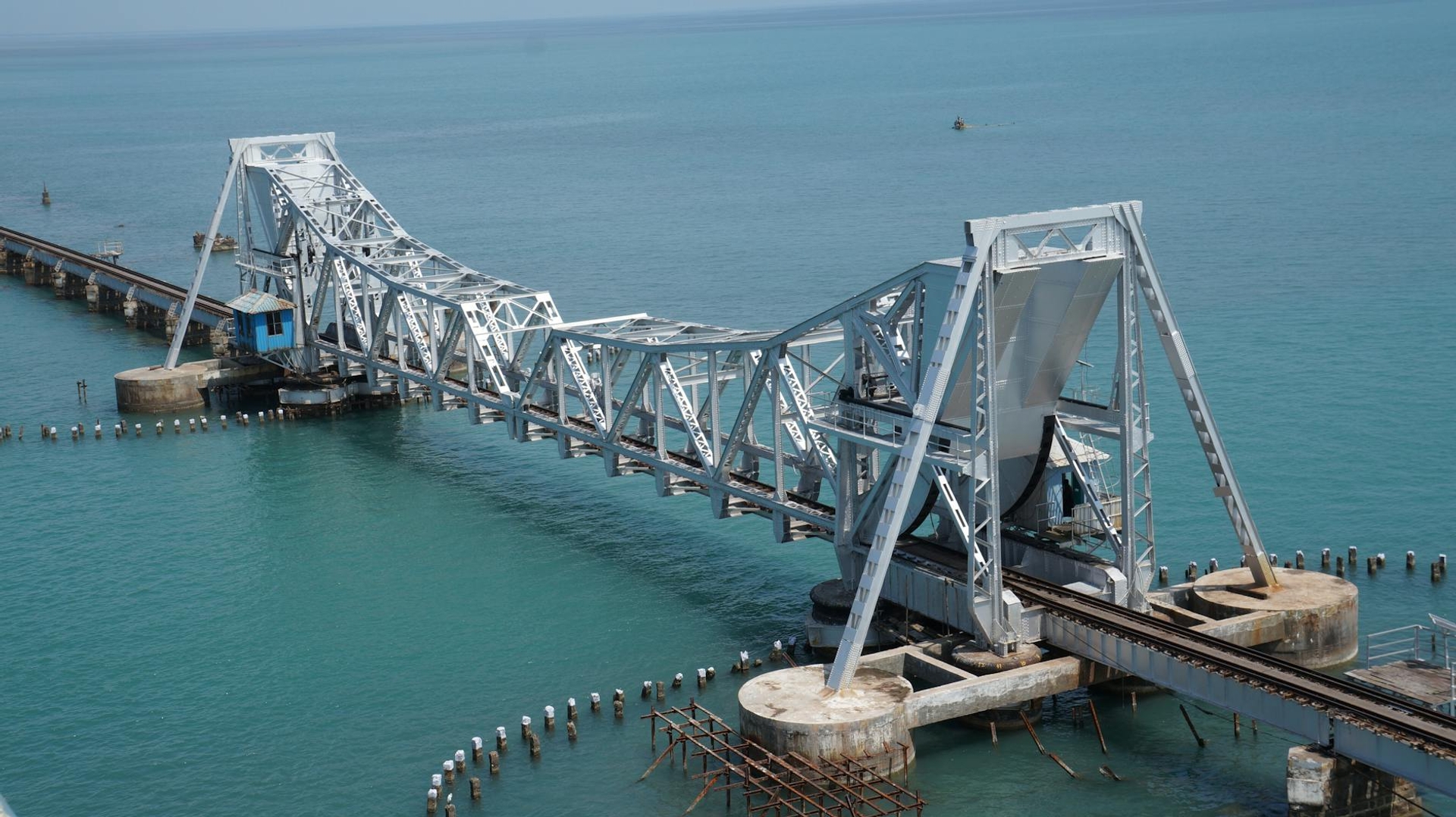 A steel truss bascule bridge raised open above turquoise coastal water