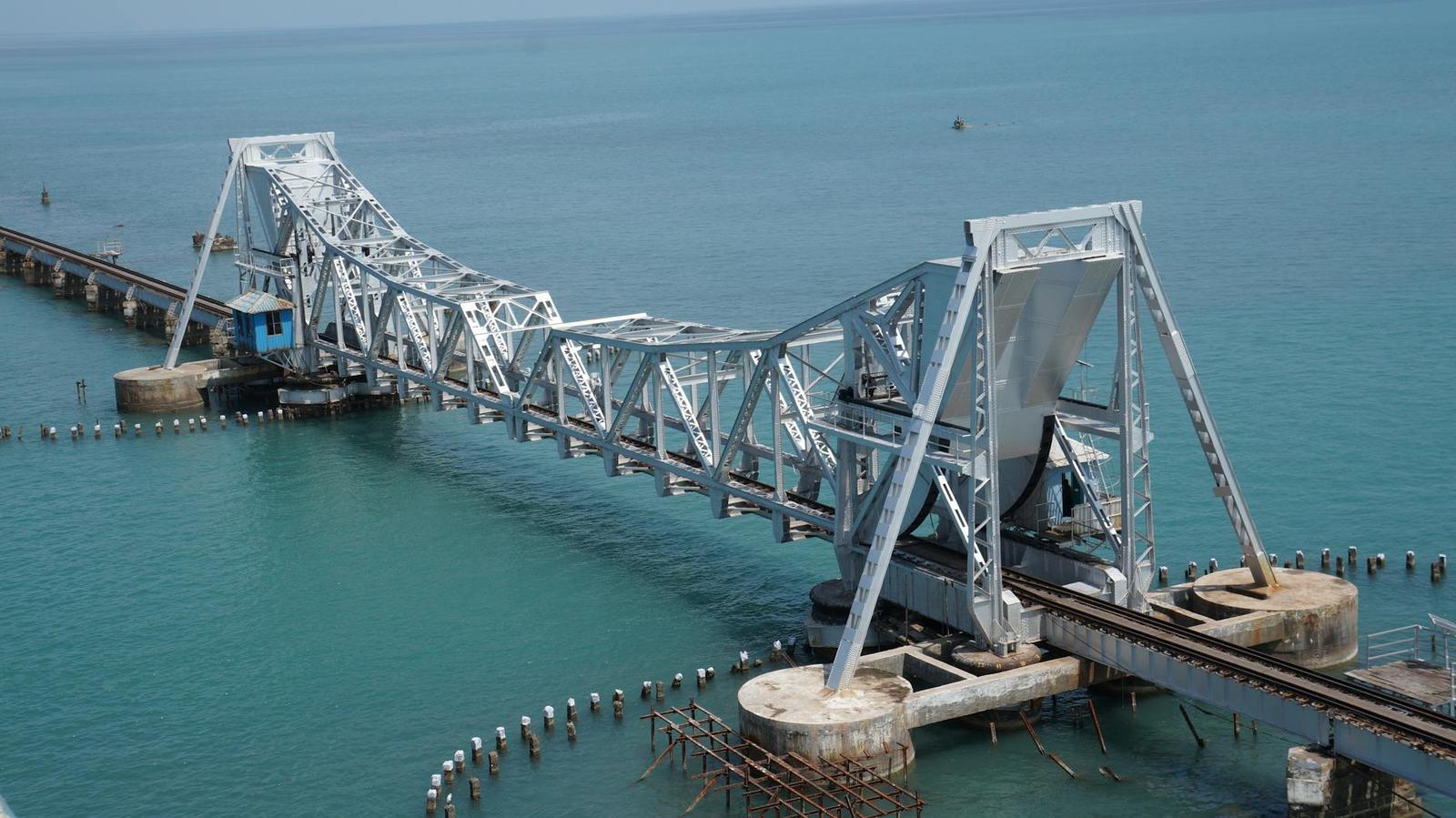 A steel truss bascule bridge raised open above turquoise coastal water
