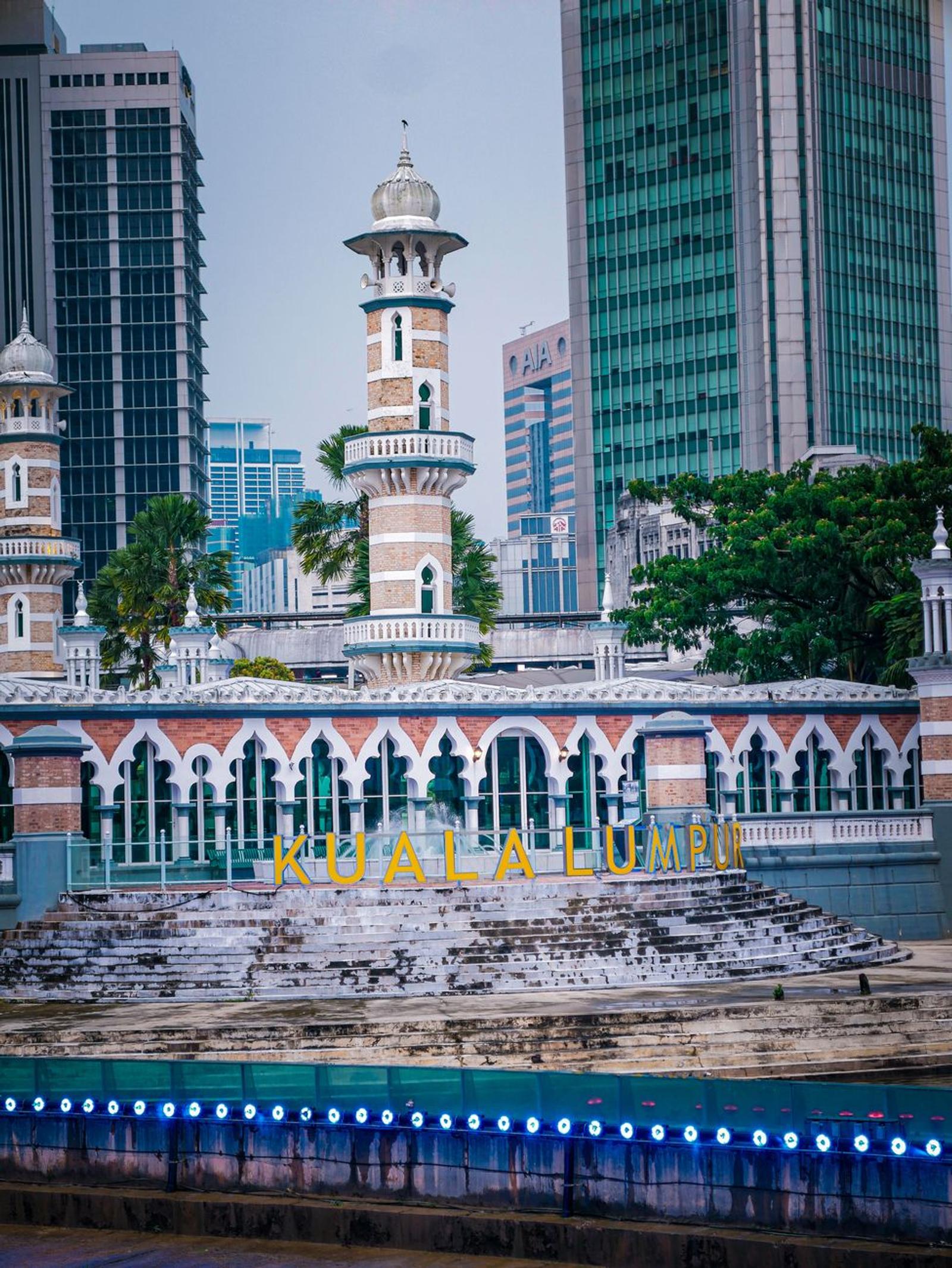 Ornate mosque minarets standing before glass office towers in a city centre
