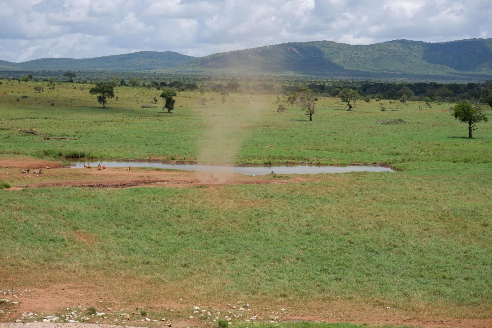 A picturesque scene of a dust devil swirling on the Kenyan savanna with distant mountains