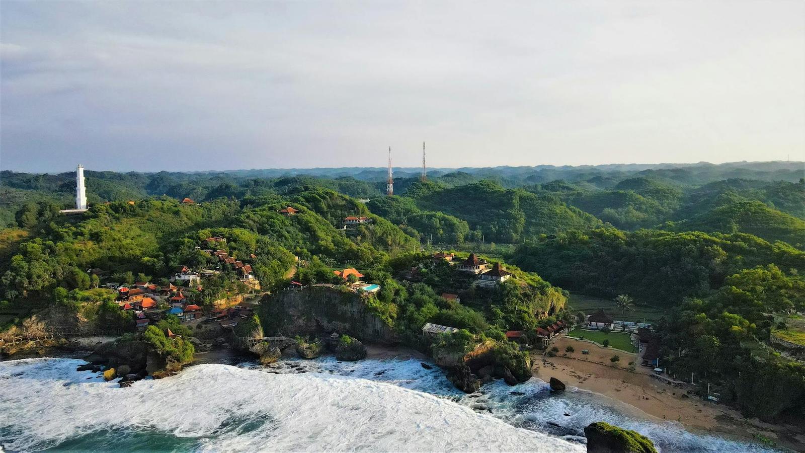 Aerial view of a cliffside village overlooking crashing waves and forest