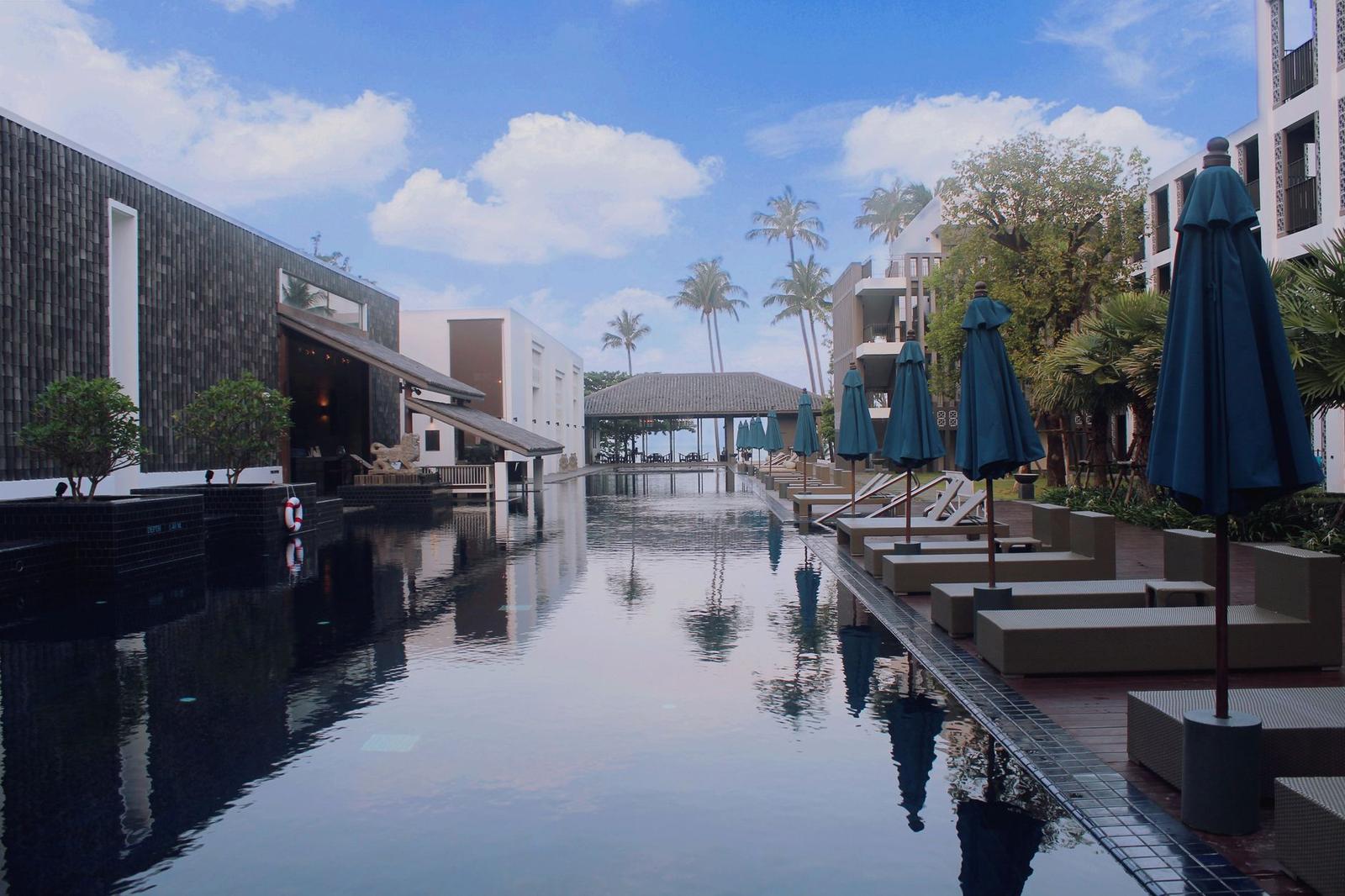 Resort pool deck lined with shaded loungers beside palm trees