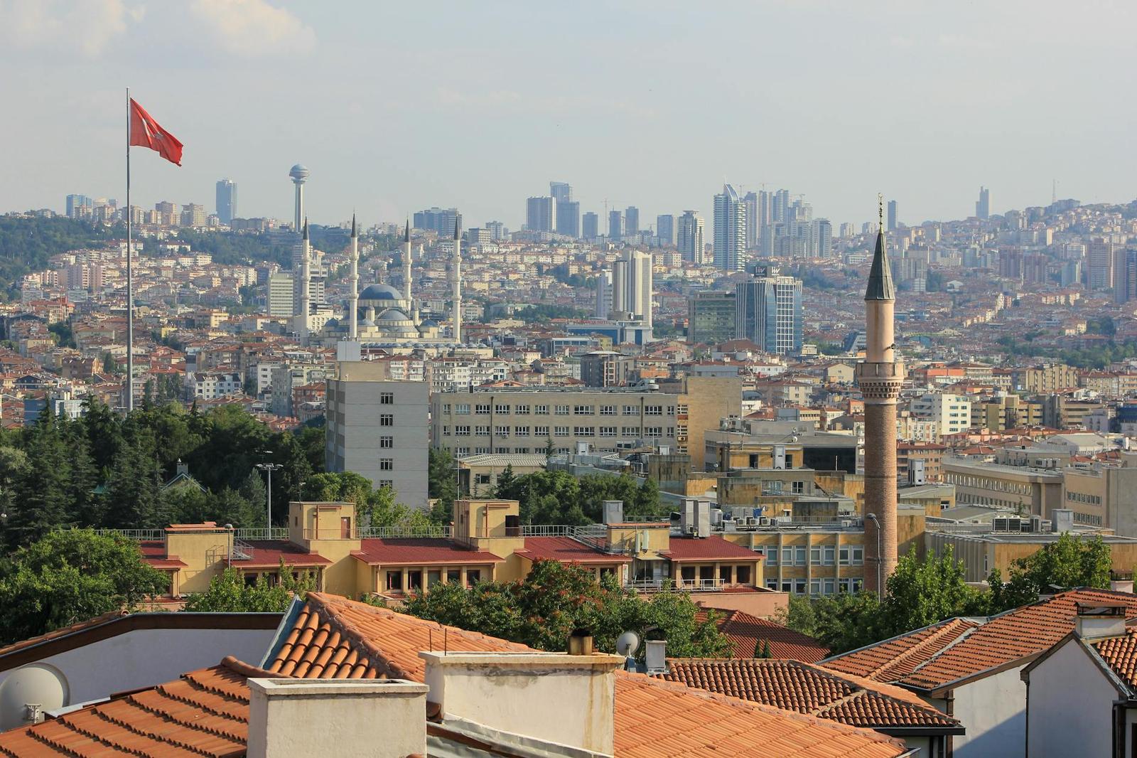 A hillside city view with a mosque, minarets and red-tiled roofs against a distant skyline