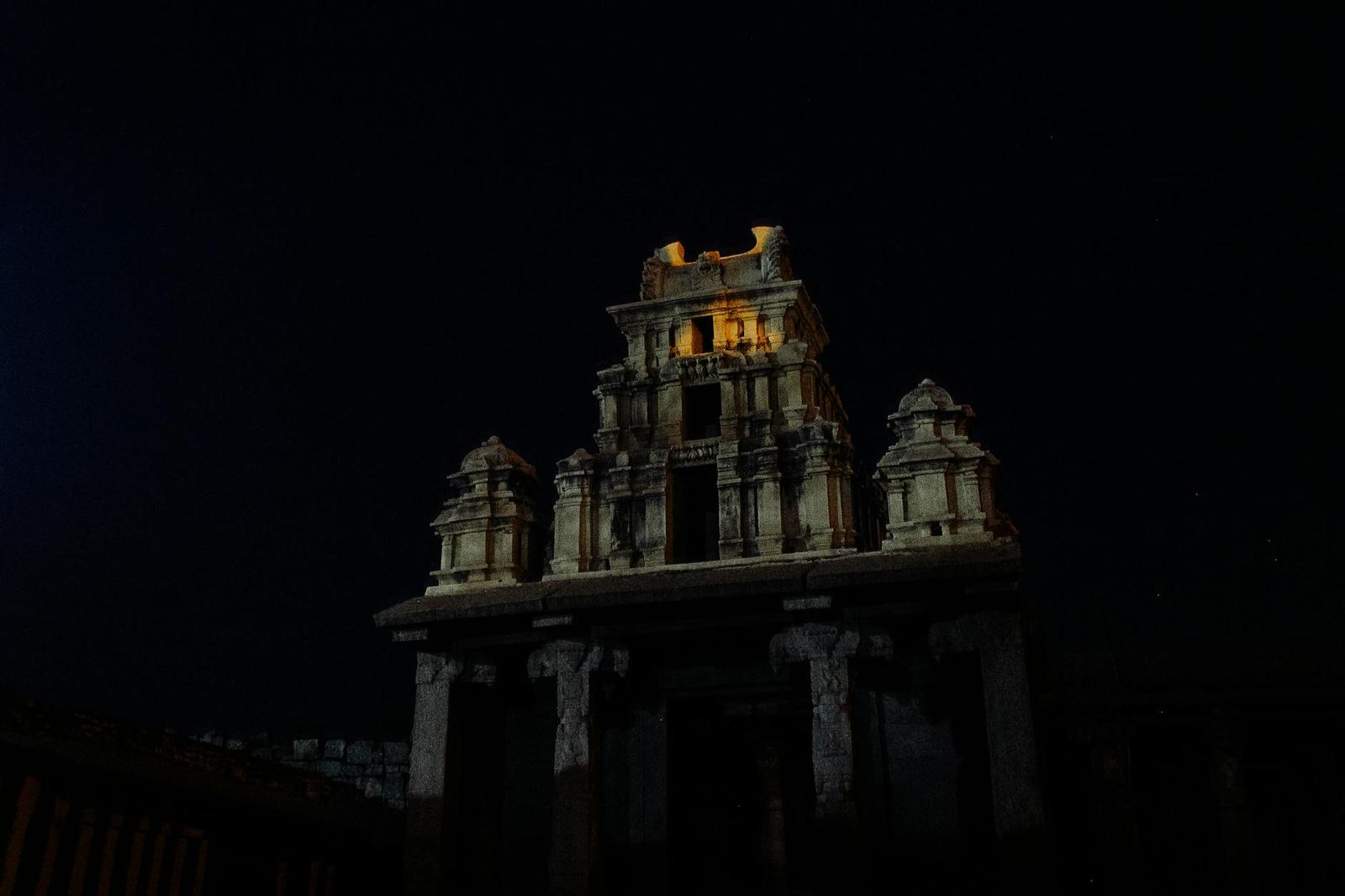 Stone temple gate tower lit up against a pitch-black night sky