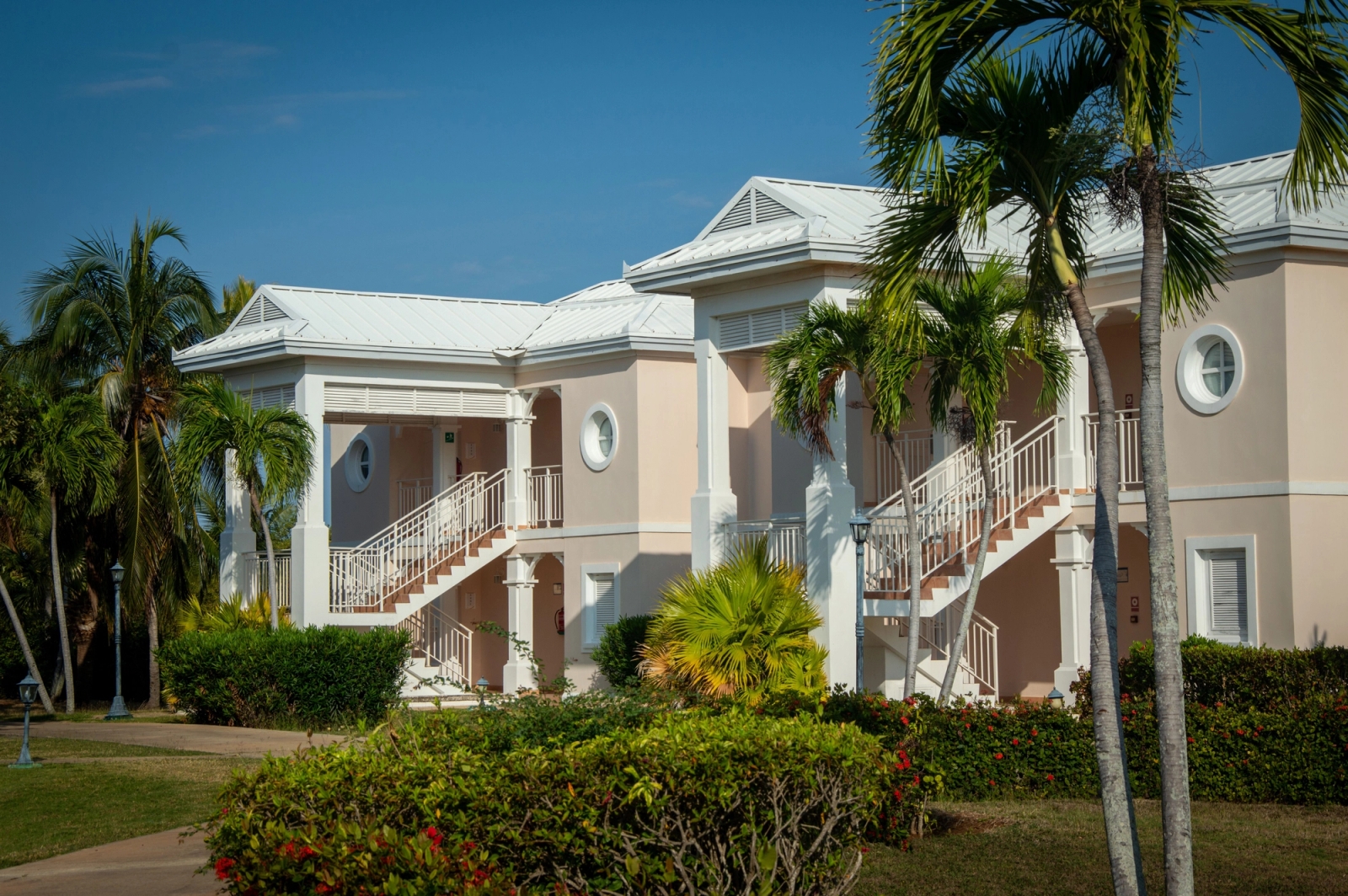Exterior view of a tropical resort with classic architecture and lush palm trees under a clear blue sky