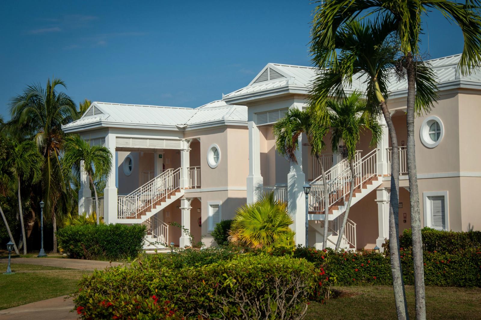 Exterior view of a tropical resort with classic architecture and lush palm trees under a clear blue sky