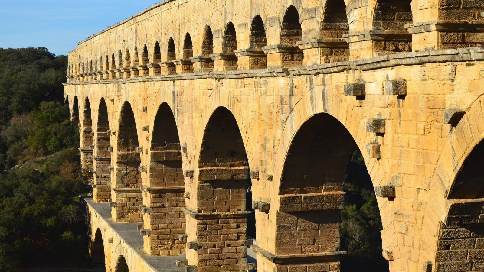 Elegant Roman aqueduct, Pont du Gard, basked in sunlight amidst lush scenery