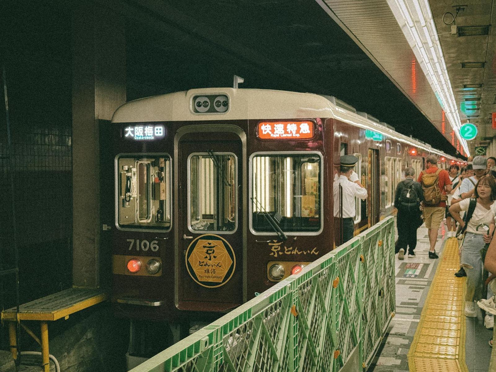 Vintage maroon train pulling into a covered station platform with waiting passengers
