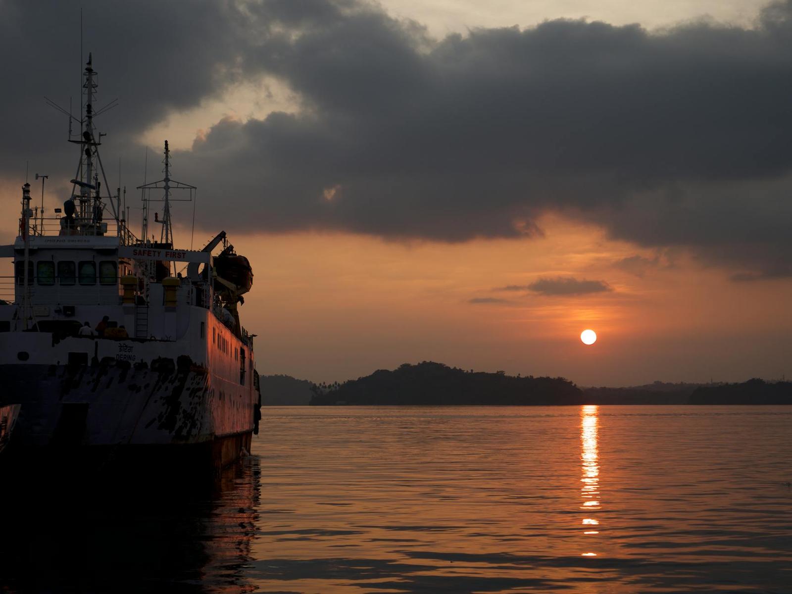 Silhouette of a docked ship against an orange sunset over calm water