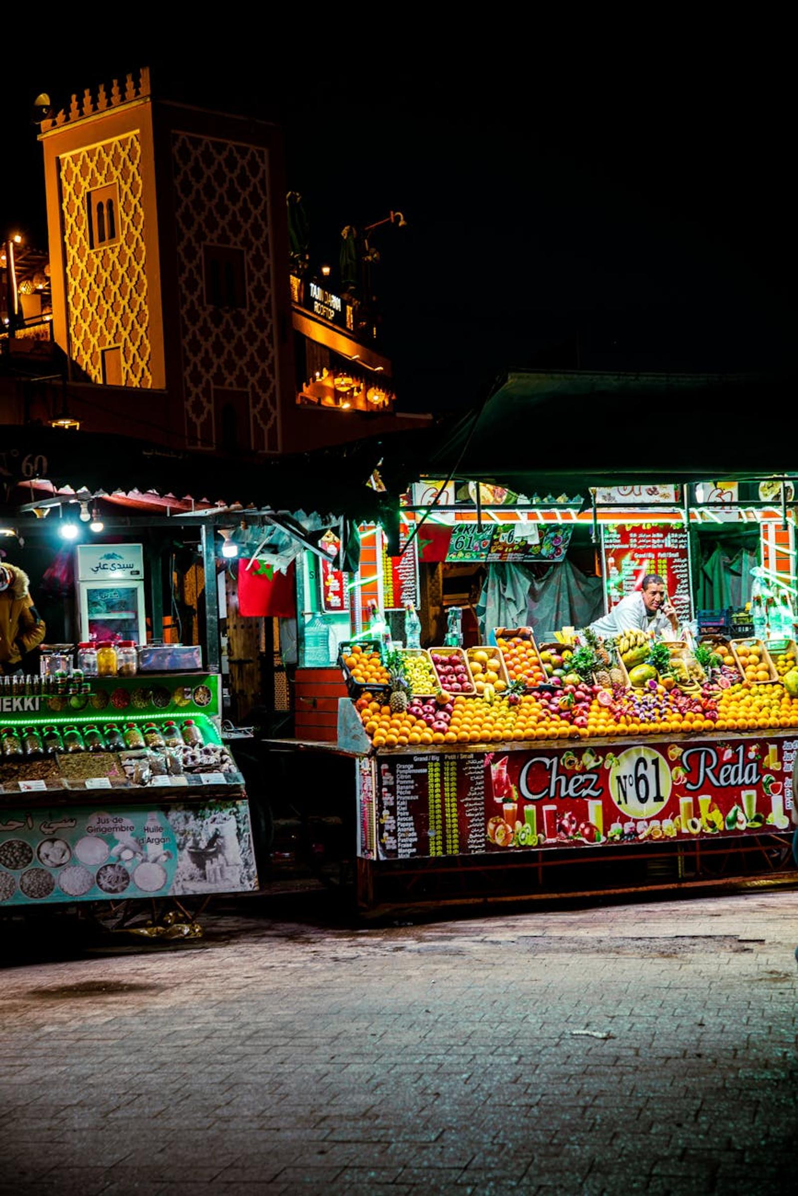 Illuminated night market stall piled with fresh oranges beside a carved gateway