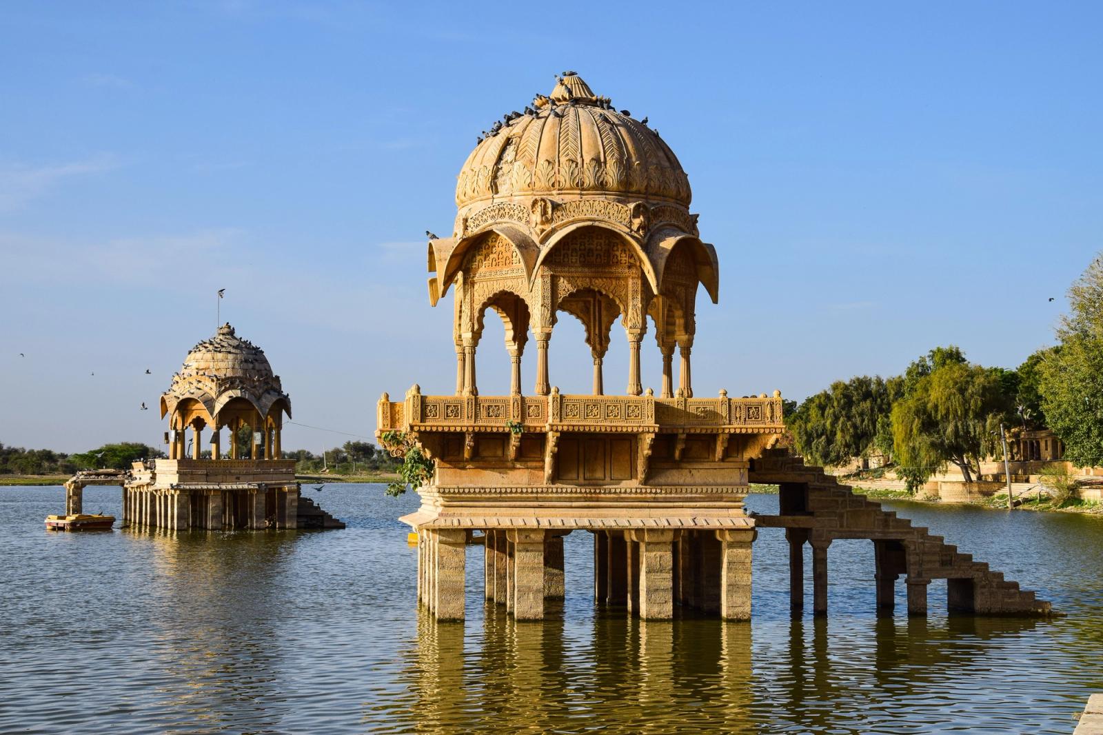 Domed sandstone pavilions rising from a still lake under a clear sky