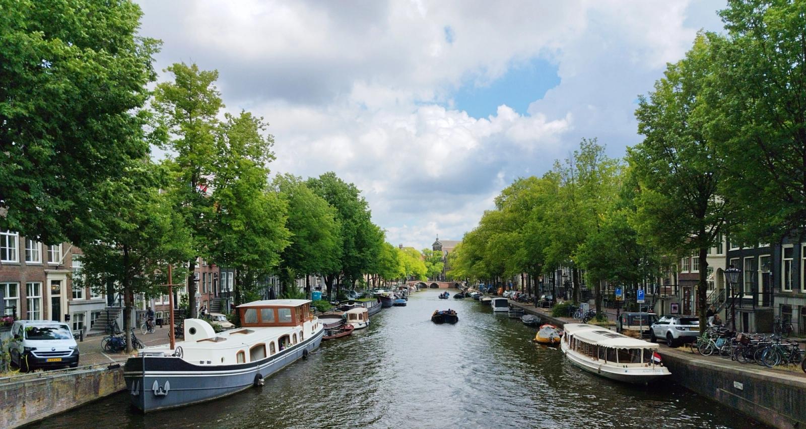 Picturesque view of Amsterdam canal with boats and lush trees under a cloudy sky