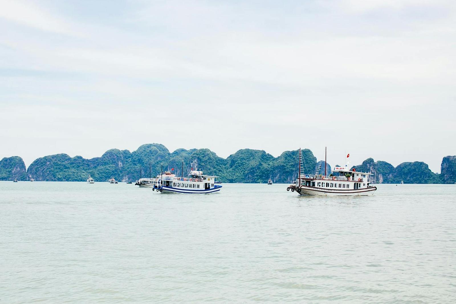 Tour boats anchored near jagged limestone islands on a calm grey sea