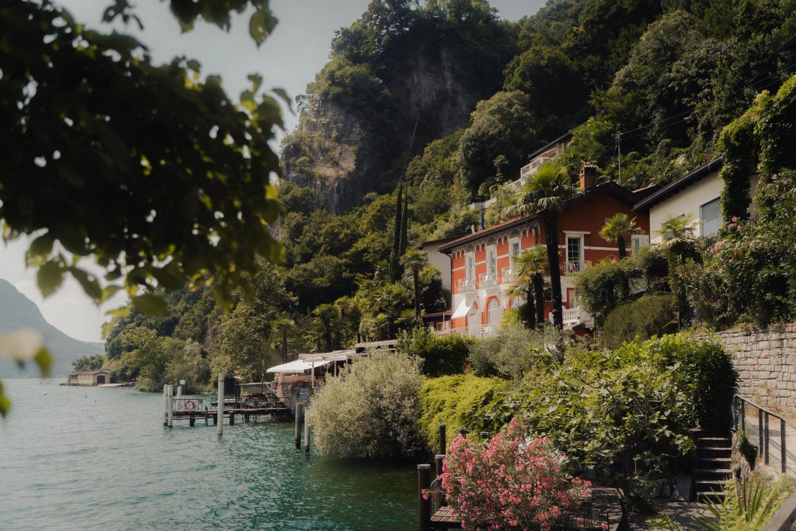 A terracotta lakeside villa nestled among trees with a jetty below