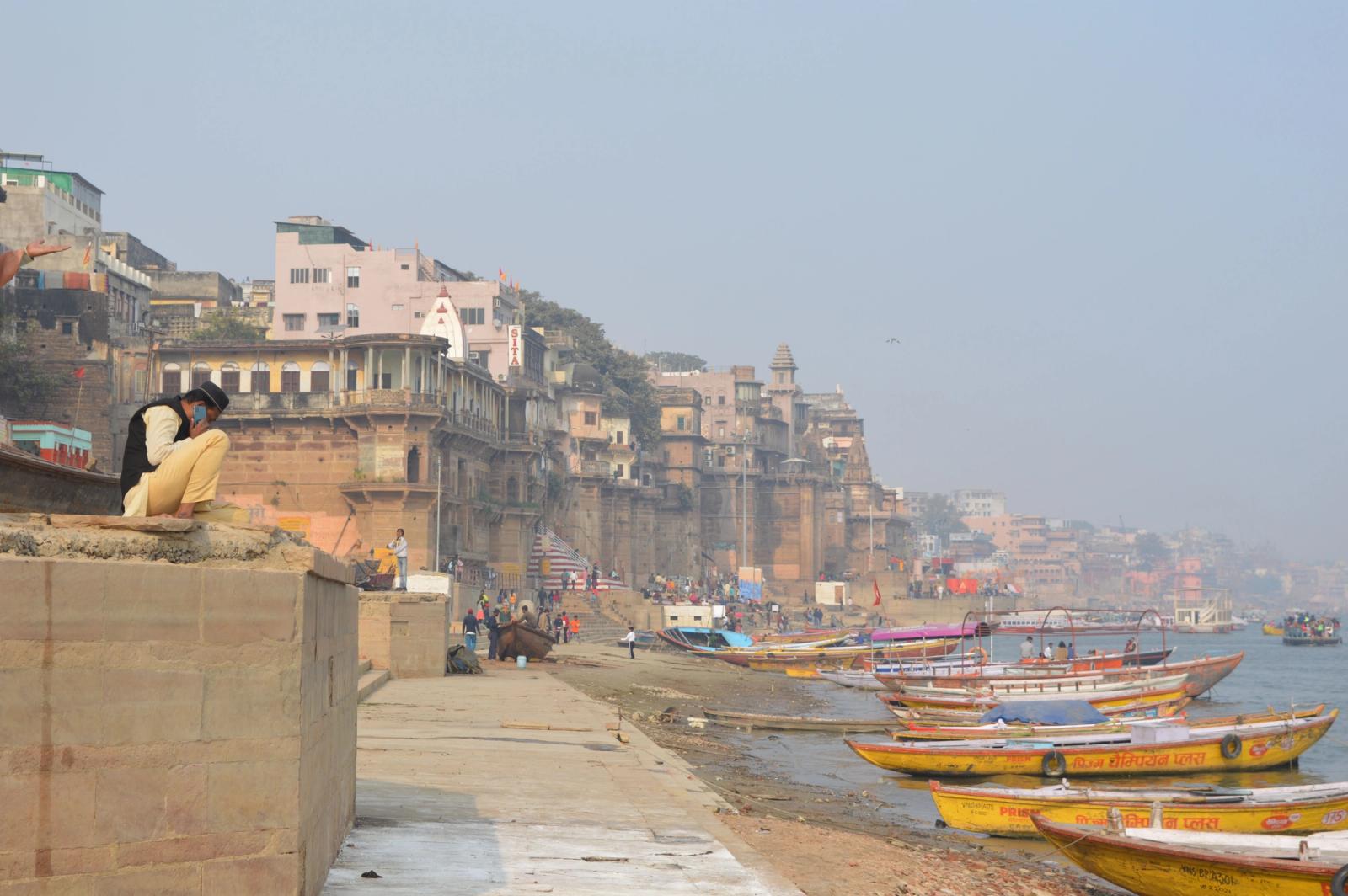 Colorful boats docked on the Ganges River, with historic Varanasi ghats and architecture in the background