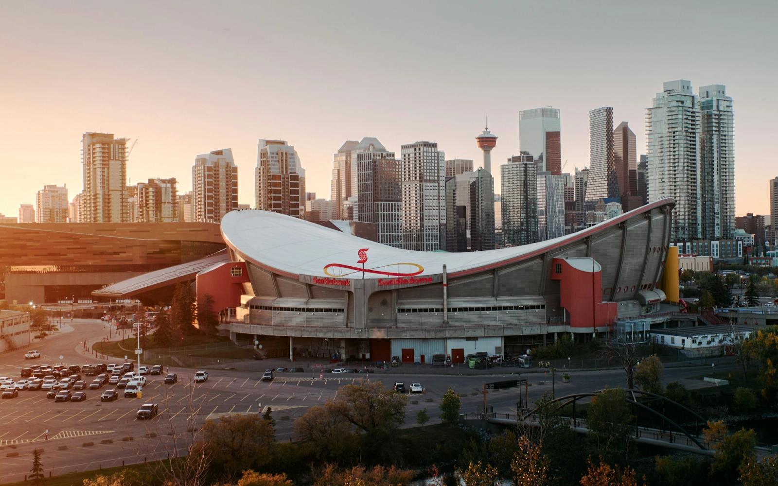 A curved white-roofed arena beside a city skyline at sunset