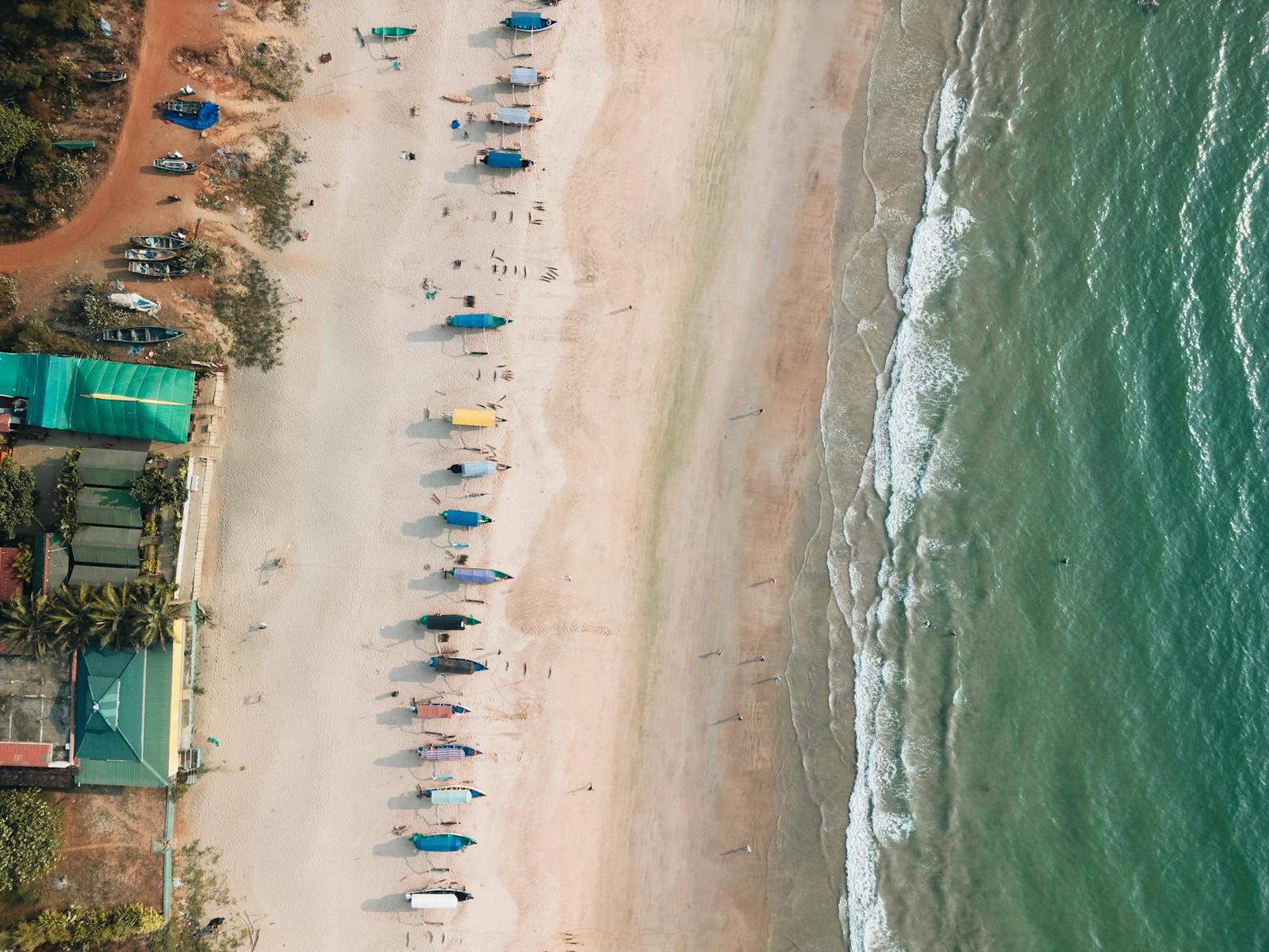 Aerial view of fishing boats lined along a sandy beach beside turquoise waves