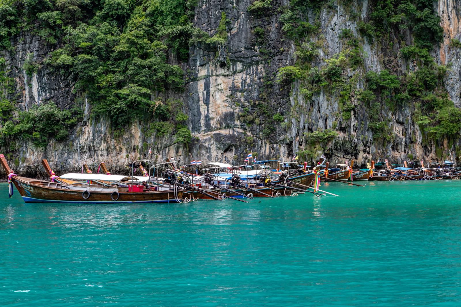 Scenic view of traditional longtail boats moored against cliffs in Phuket, Thailand's turquoise waters